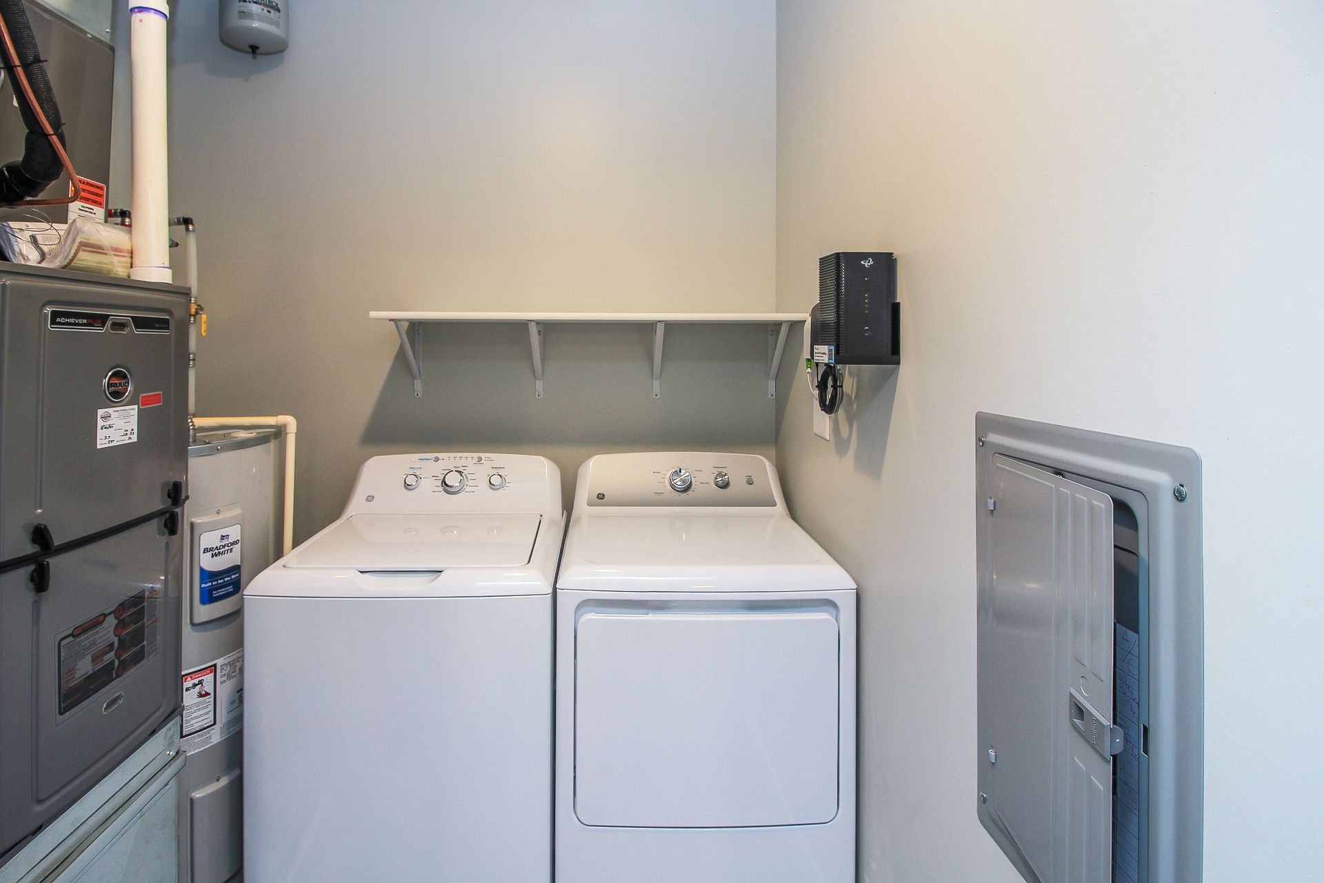 Laundry room with a washer and dryer, shelf above, and utility panels on the walls.