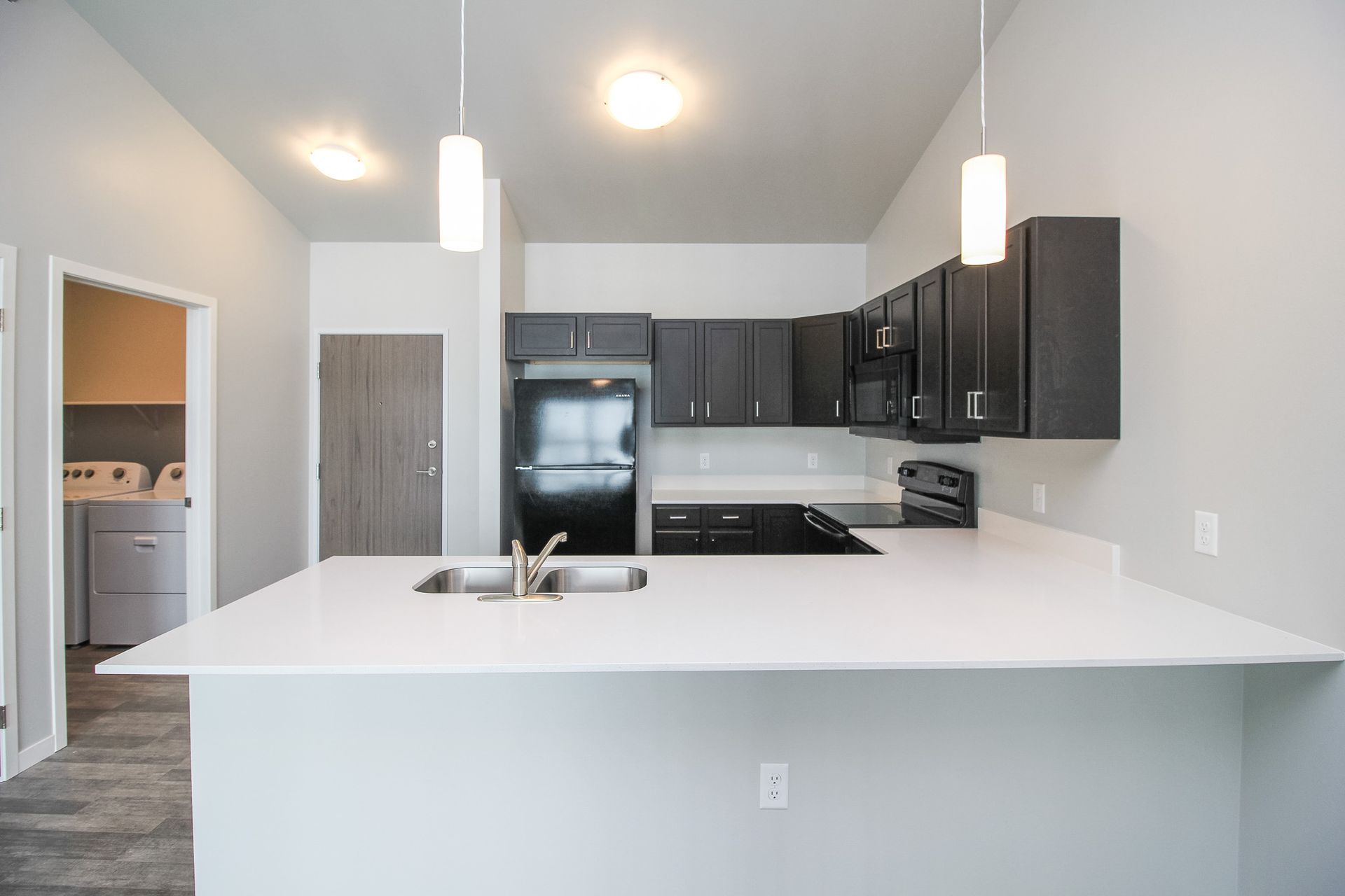 Modern white kitchen with island, pendant lights, dark cabinets, and stainless steel appliances