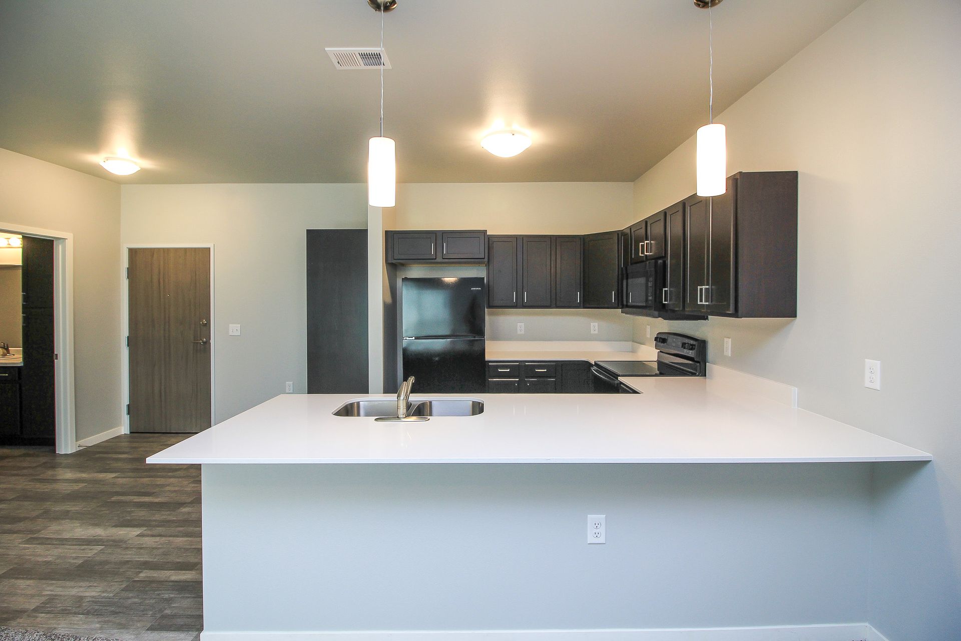 Modern apartment kitchen with white island, dark cabinets, stainless appliances, and pendant lights