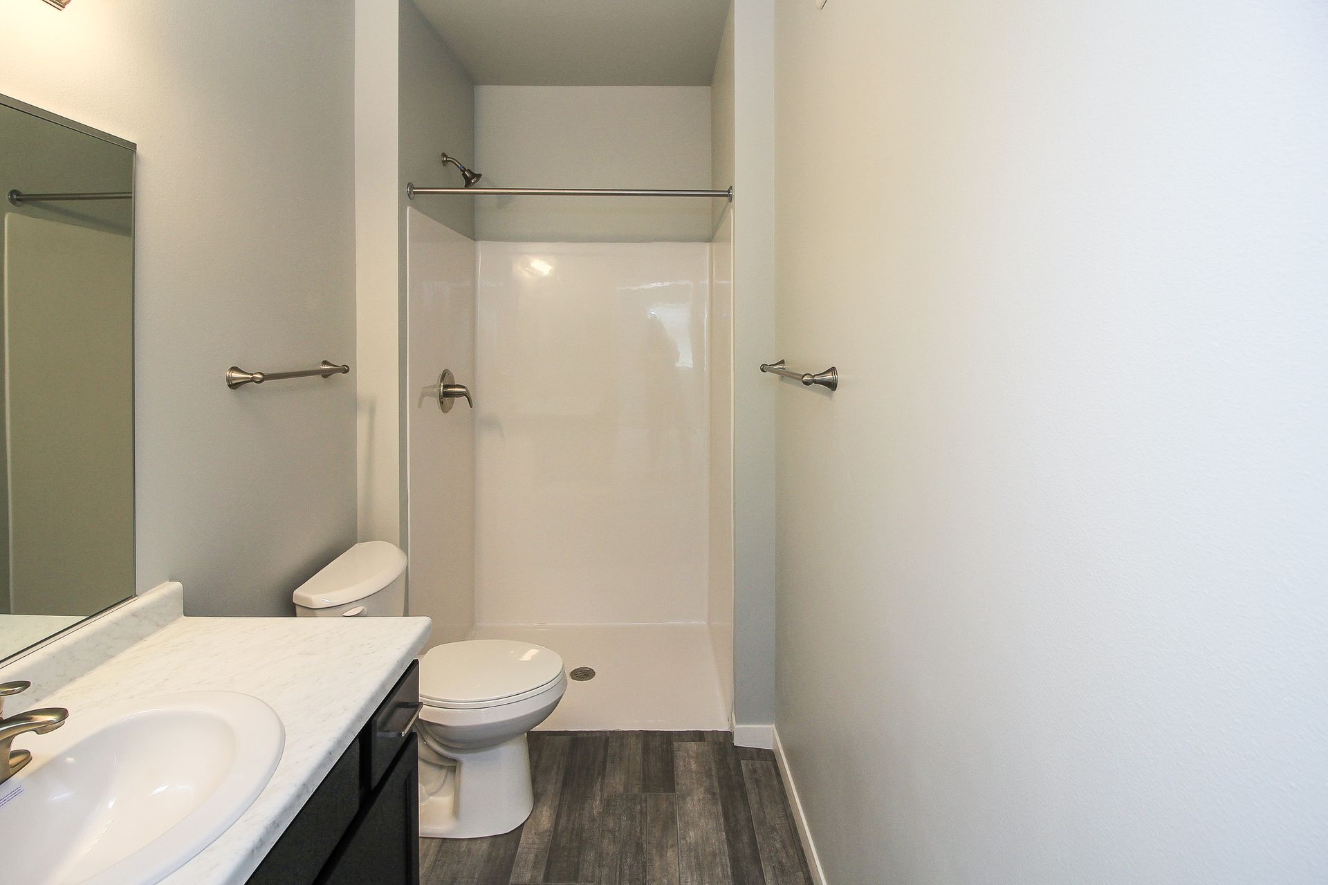 Small bathroom with toilet, sink, shower, and gray wood-look flooring