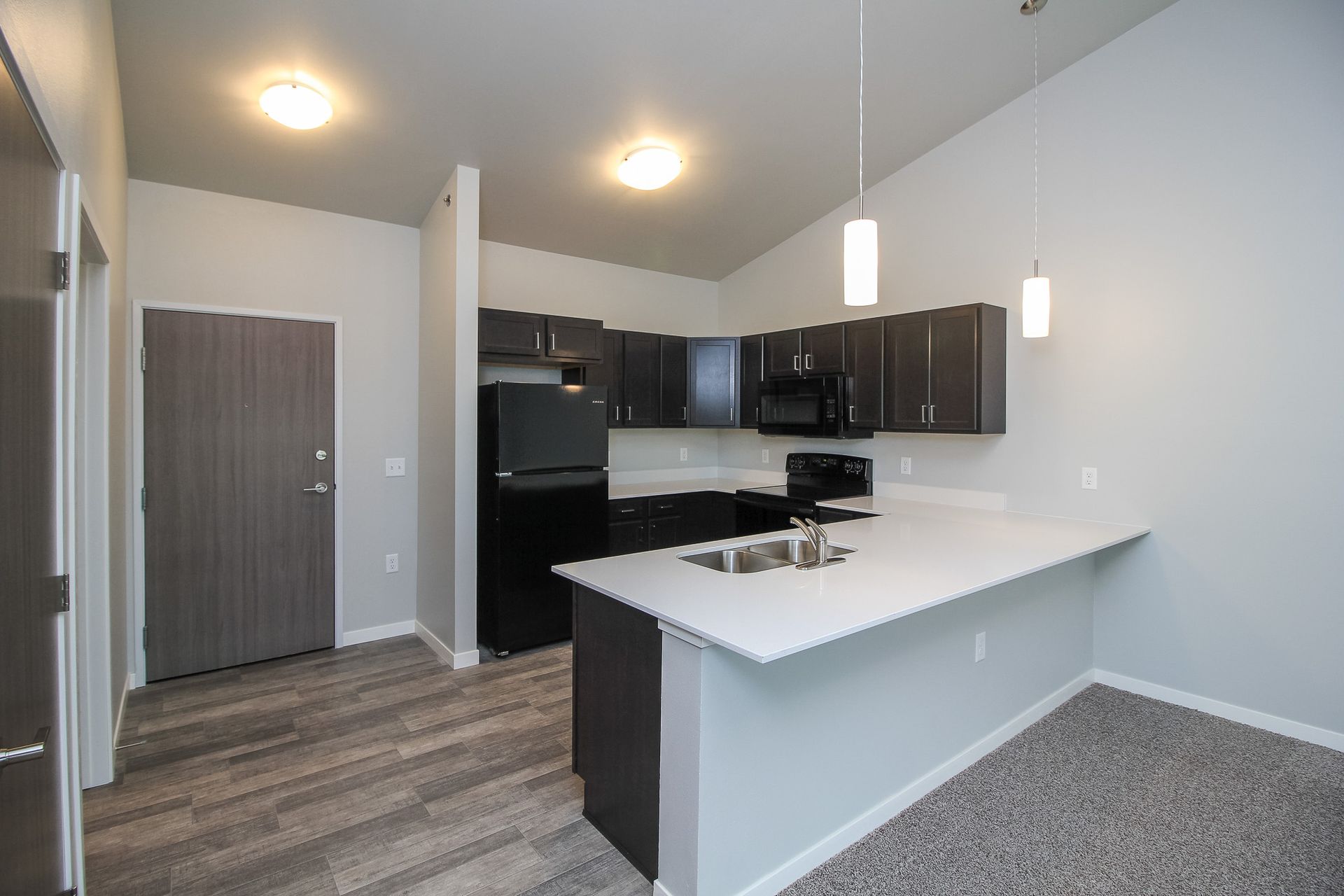 Modern kitchen with dark cabinets, white island, black appliances, and gray flooring