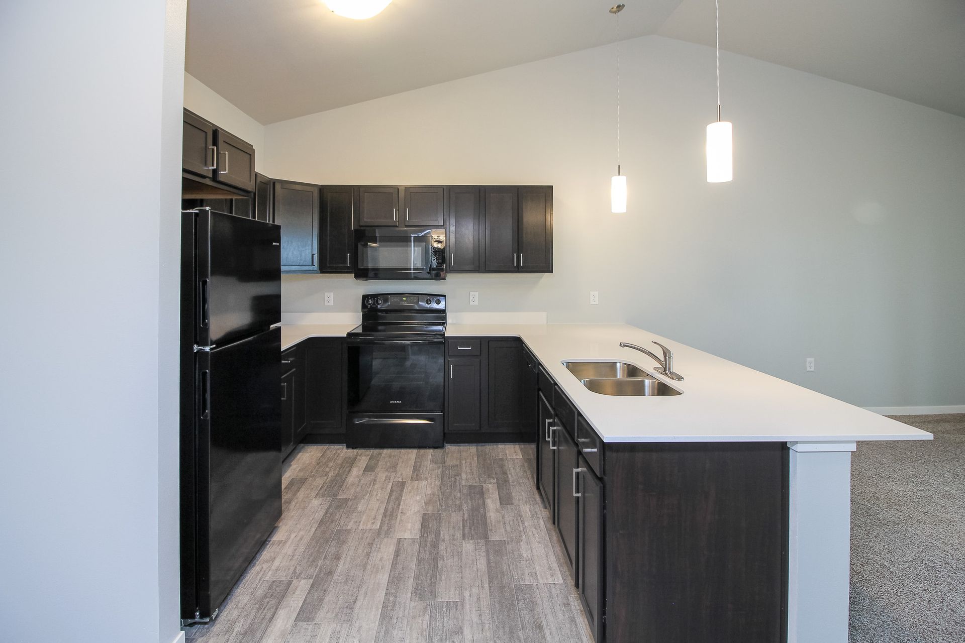 Modern kitchen with black cabinets, black appliances, gray floor, and white island countertop.