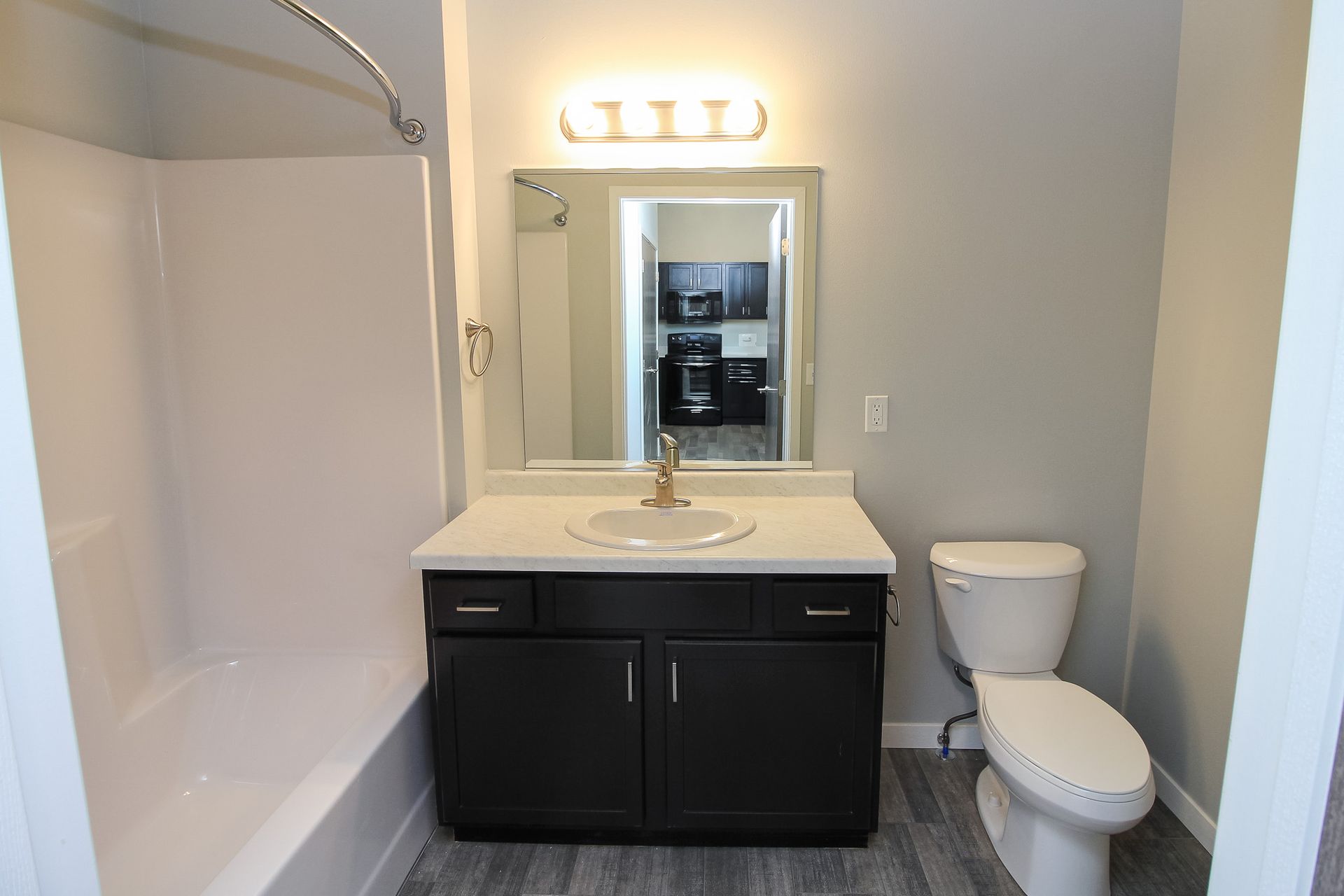 Small bathroom with vanity, mirror, light fixture, toilet, and white bathtub/shower.