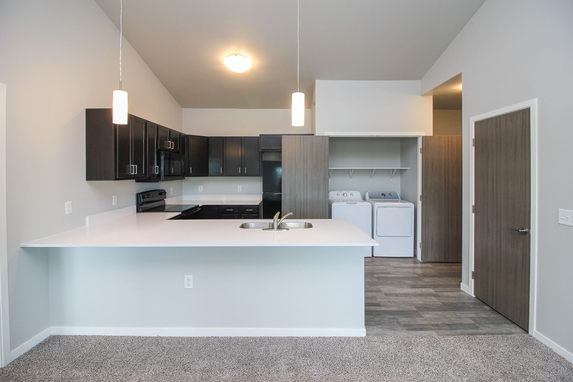 Modern open-plan kitchen with dark cabinets, white island, and pendant lights