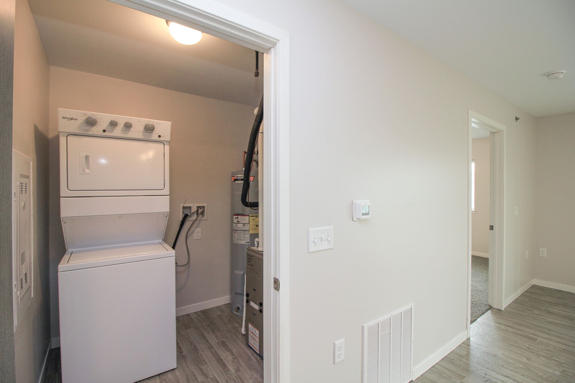 Laundry closet with stacked washer and dryer beside a hallway in a light-colored apartment
