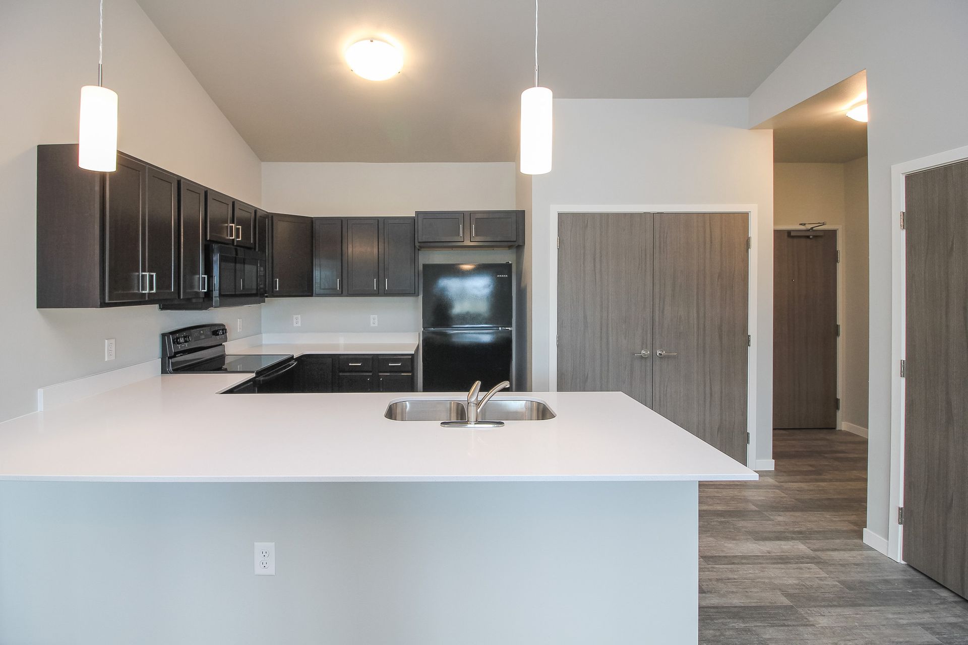 Modern kitchen with white island, dark cabinets, stainless appliances, and pendant lights