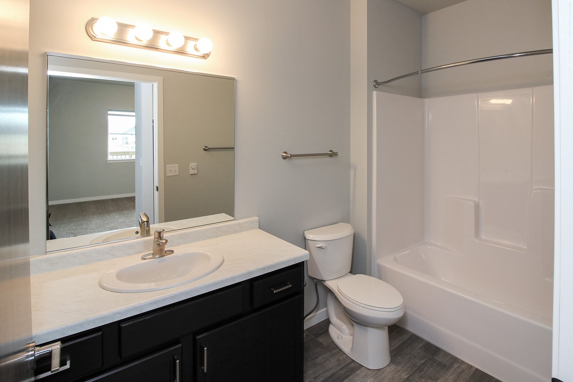Modern bathroom with white tub, toilet, dark vanity, and large mirror with lights