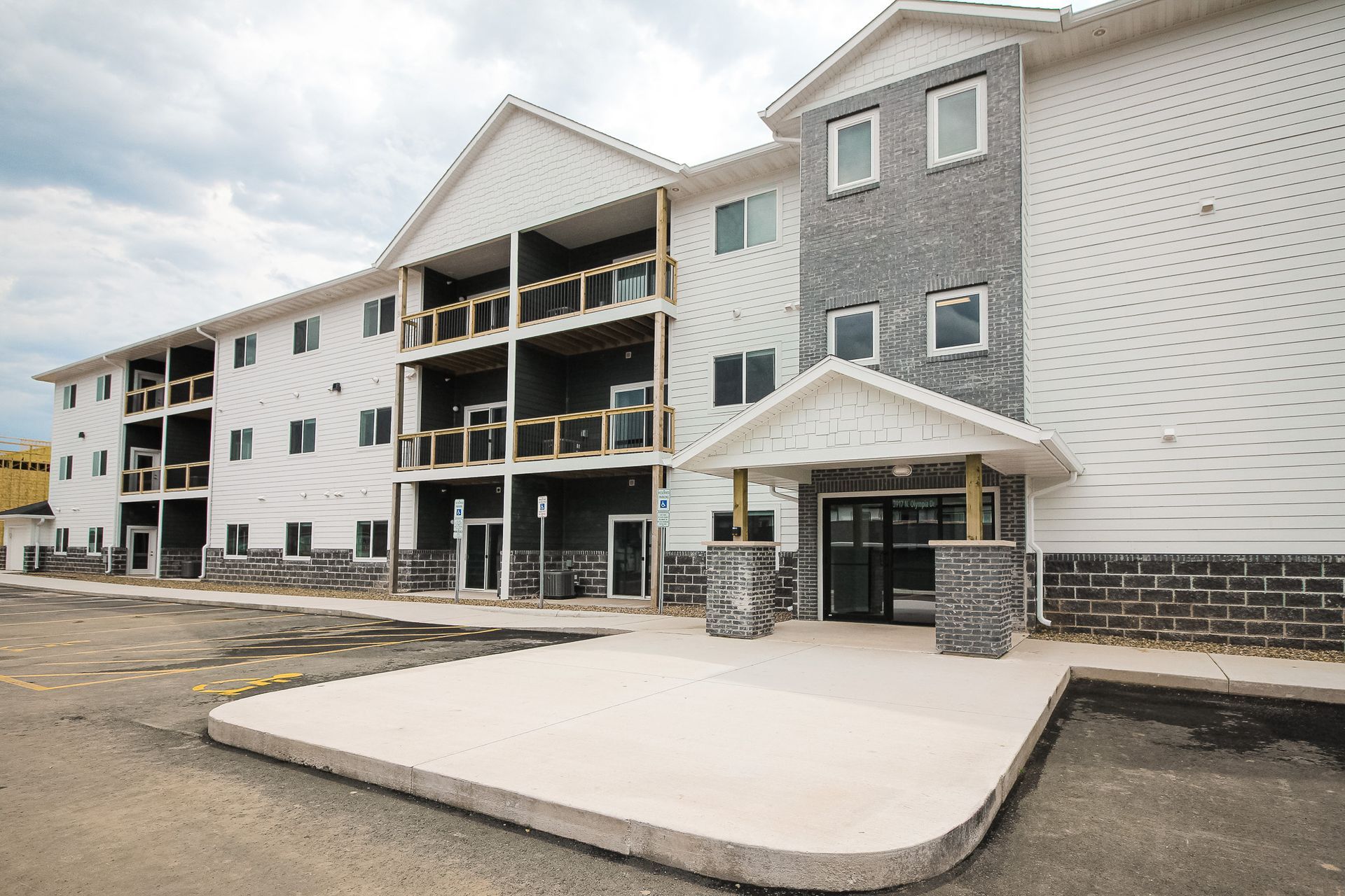 Apartment complex entrance with white and gray exterior and a concrete sidewalk under construction