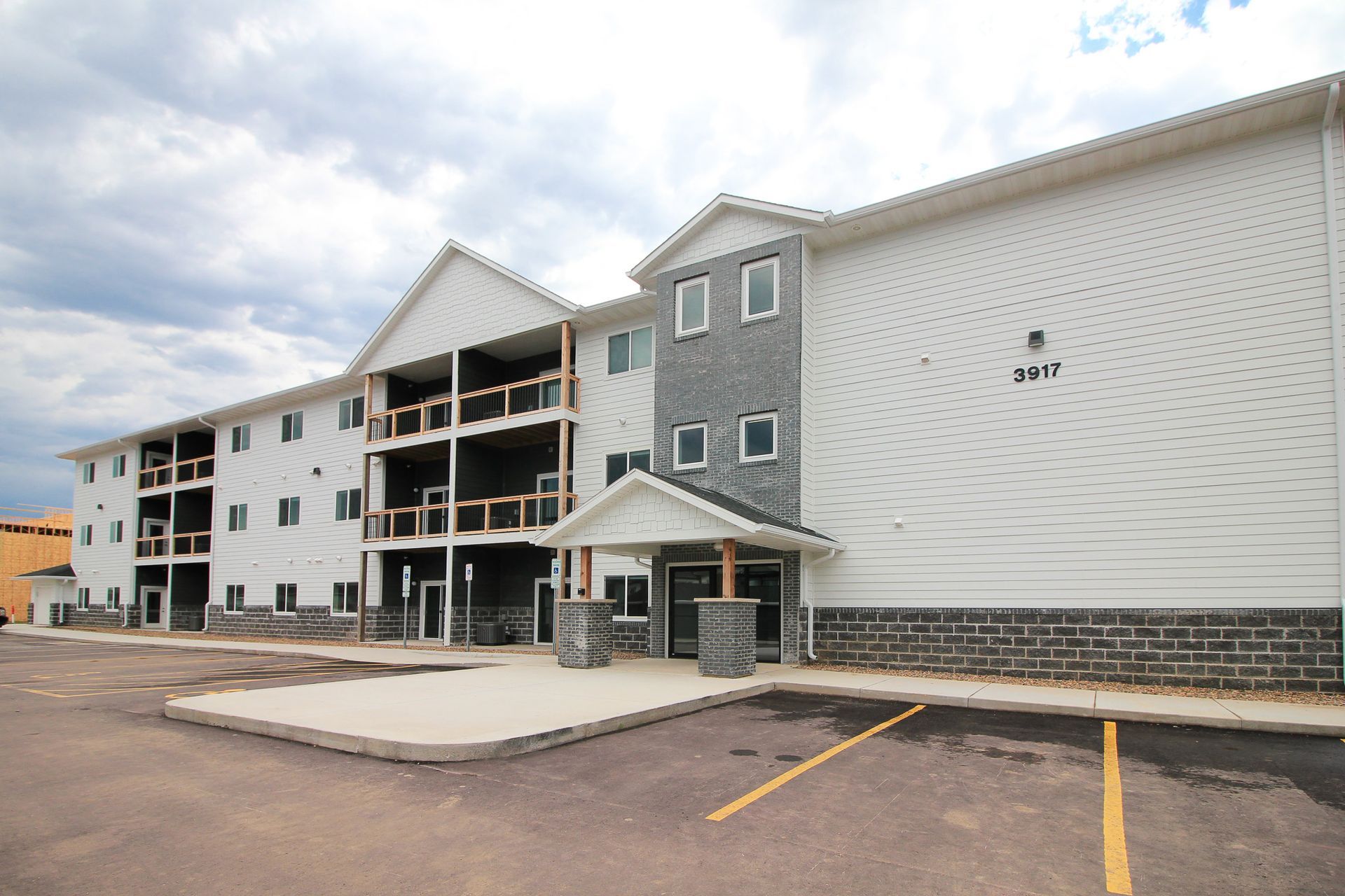 Exterior of a modern apartment building with balconies, stone accents, and empty parking lot