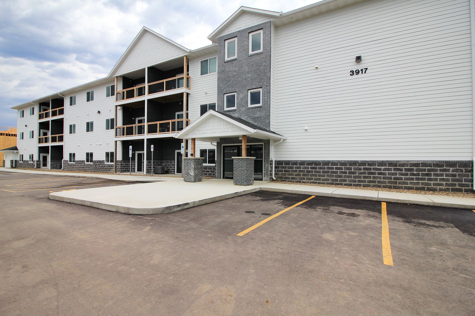 Apartment building exterior with white and gray siding, covered entrance, and empty parking lot