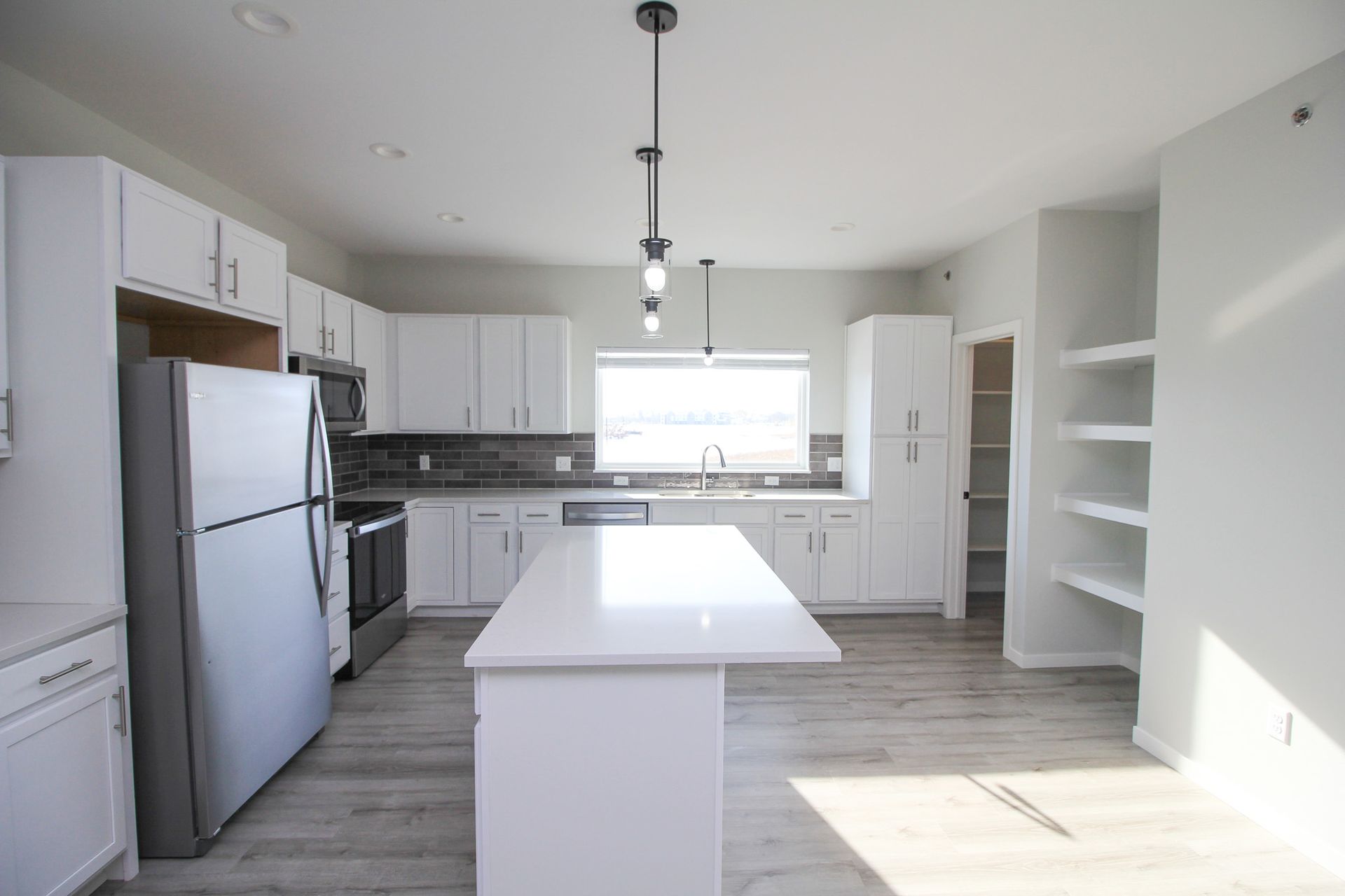 Bright white kitchen with island, stainless steel appliances, and open shelving, lit by sunlight.