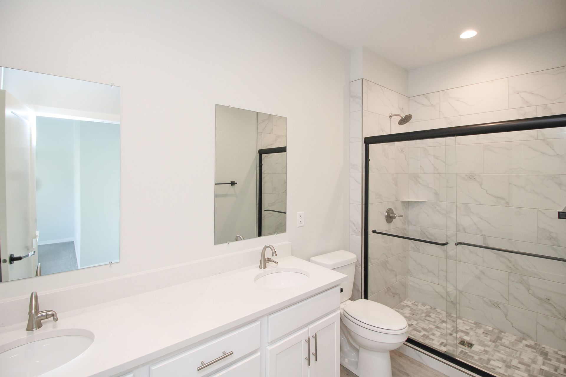 Bright modern bathroom with white vanity, mirrors, and glass walk-in shower with marble walls