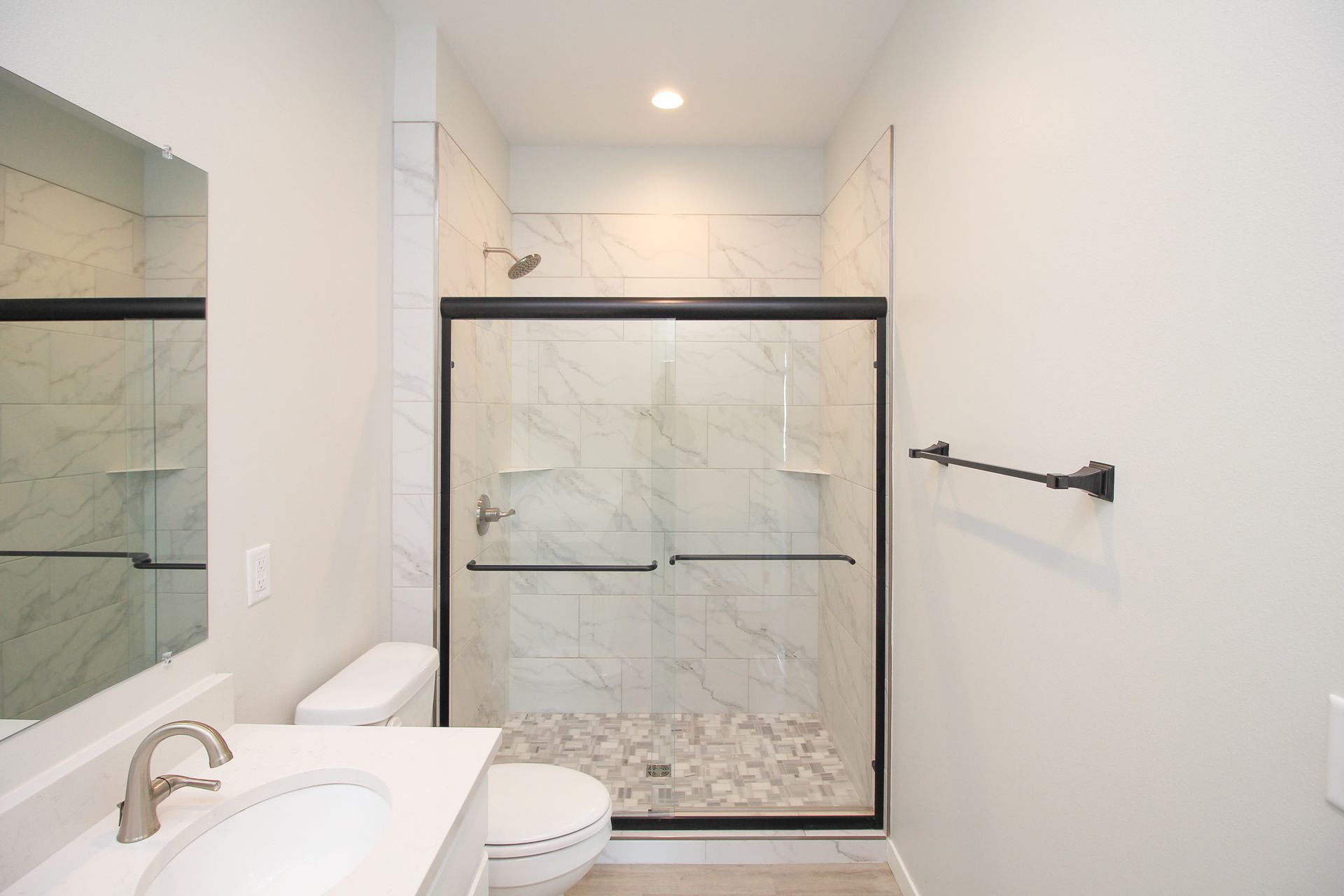 Modern white bathroom with glass shower, marble tile, white sink, and towel bar