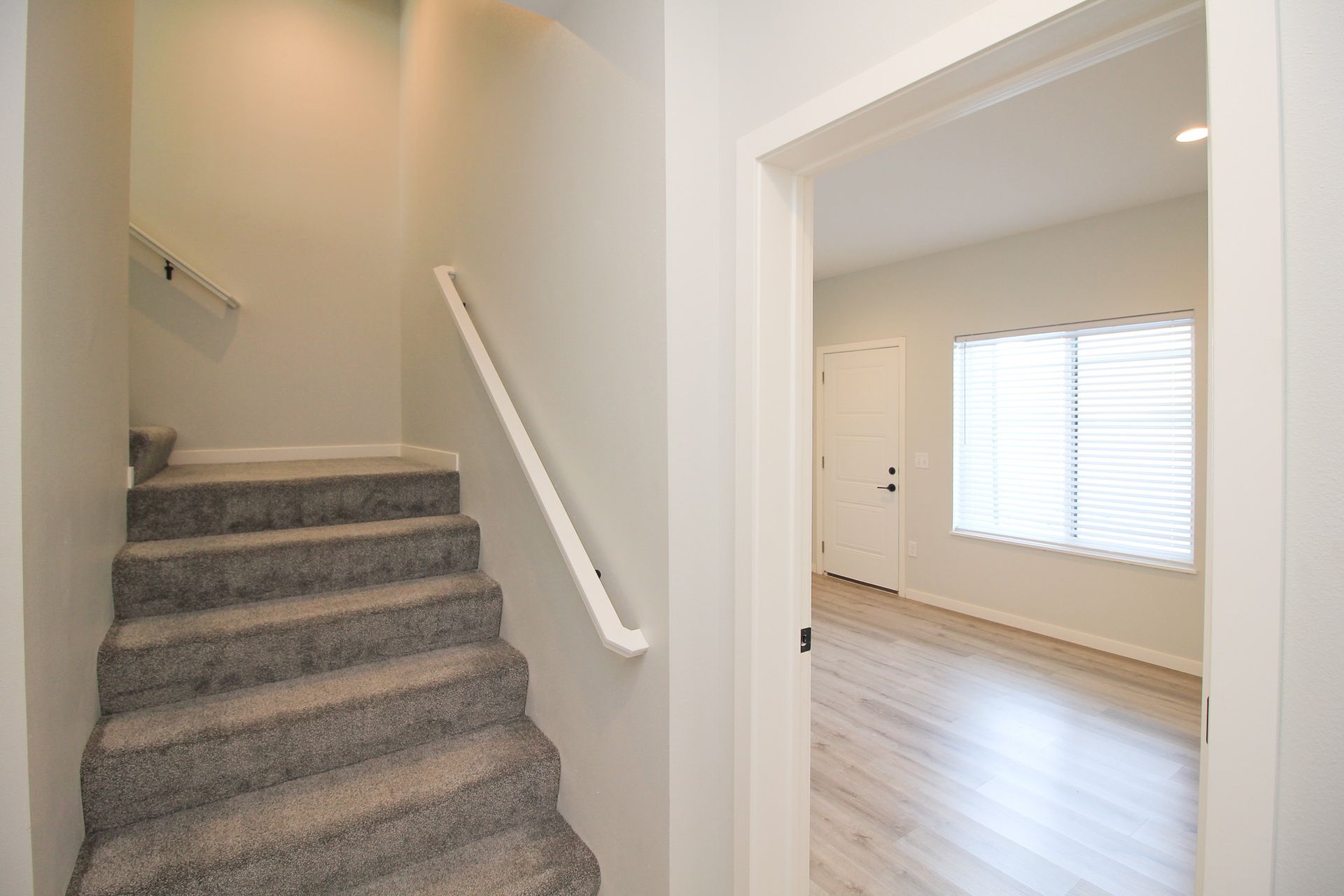 Stairway beside an open doorway to a bright room with wood floors and white blinds