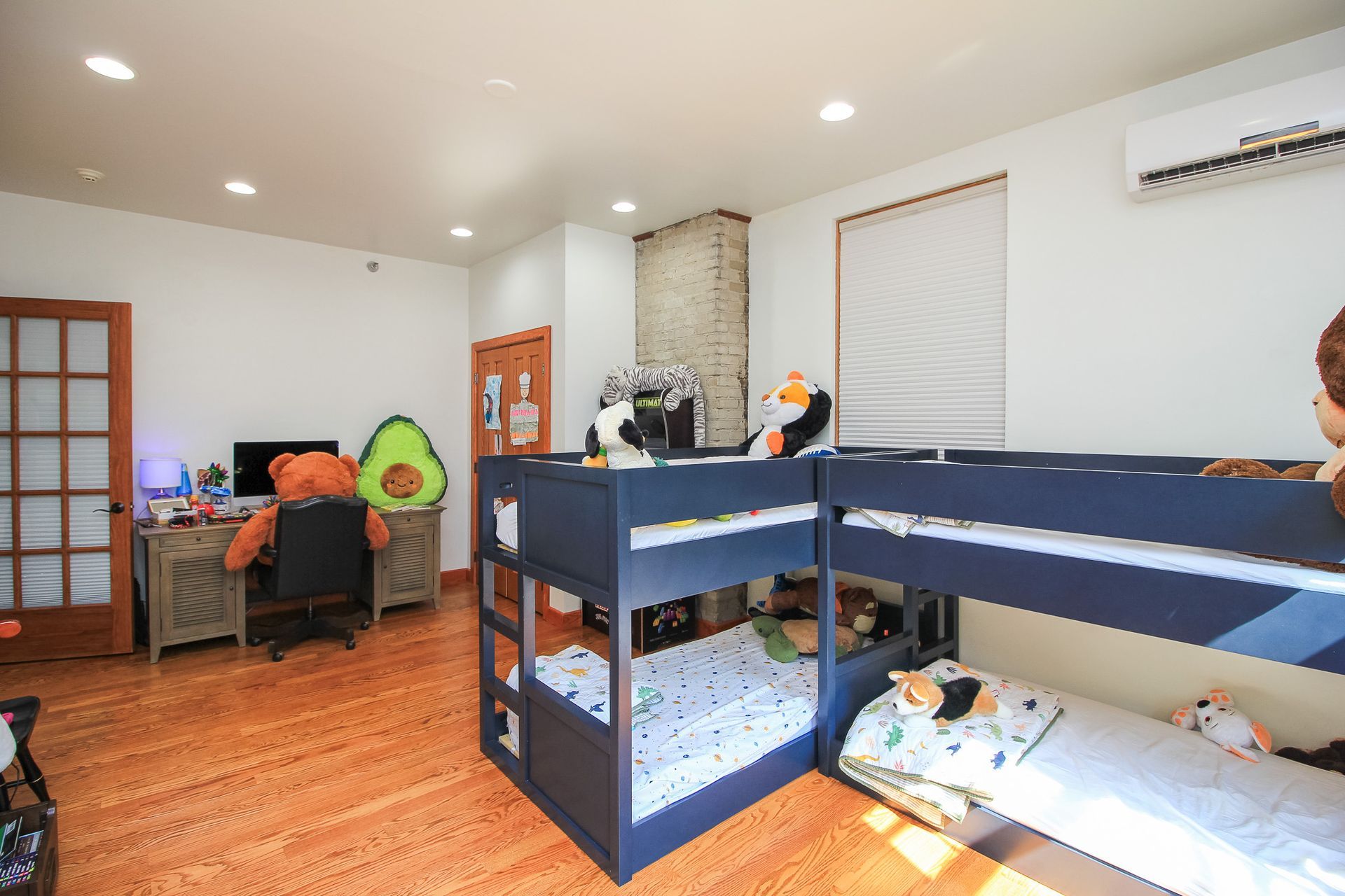 Bright bedroom with bunk bed, desk, and colorful stuffed animals on a wood floor