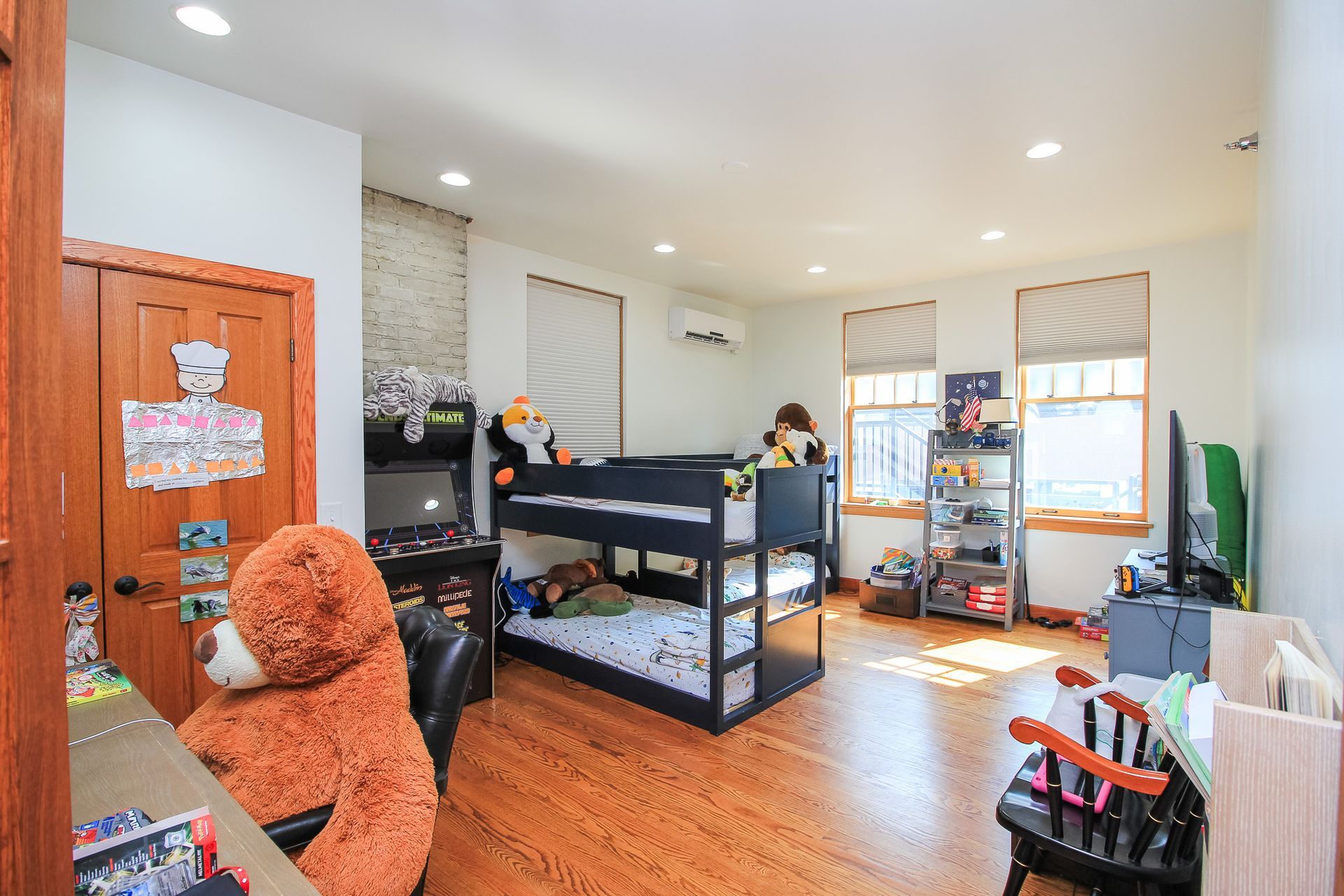 Bright bedroom with bunk bed, teddy bear chair, wooden floor, and open door to hallway