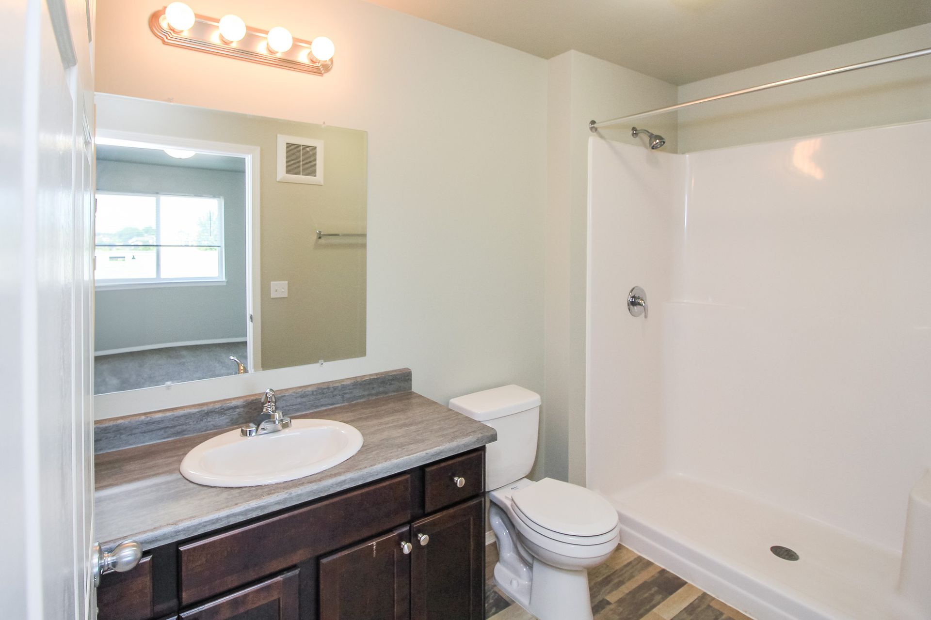 Bathroom with sink vanity, toilet, and white shower/tub surround, viewed from the doorway