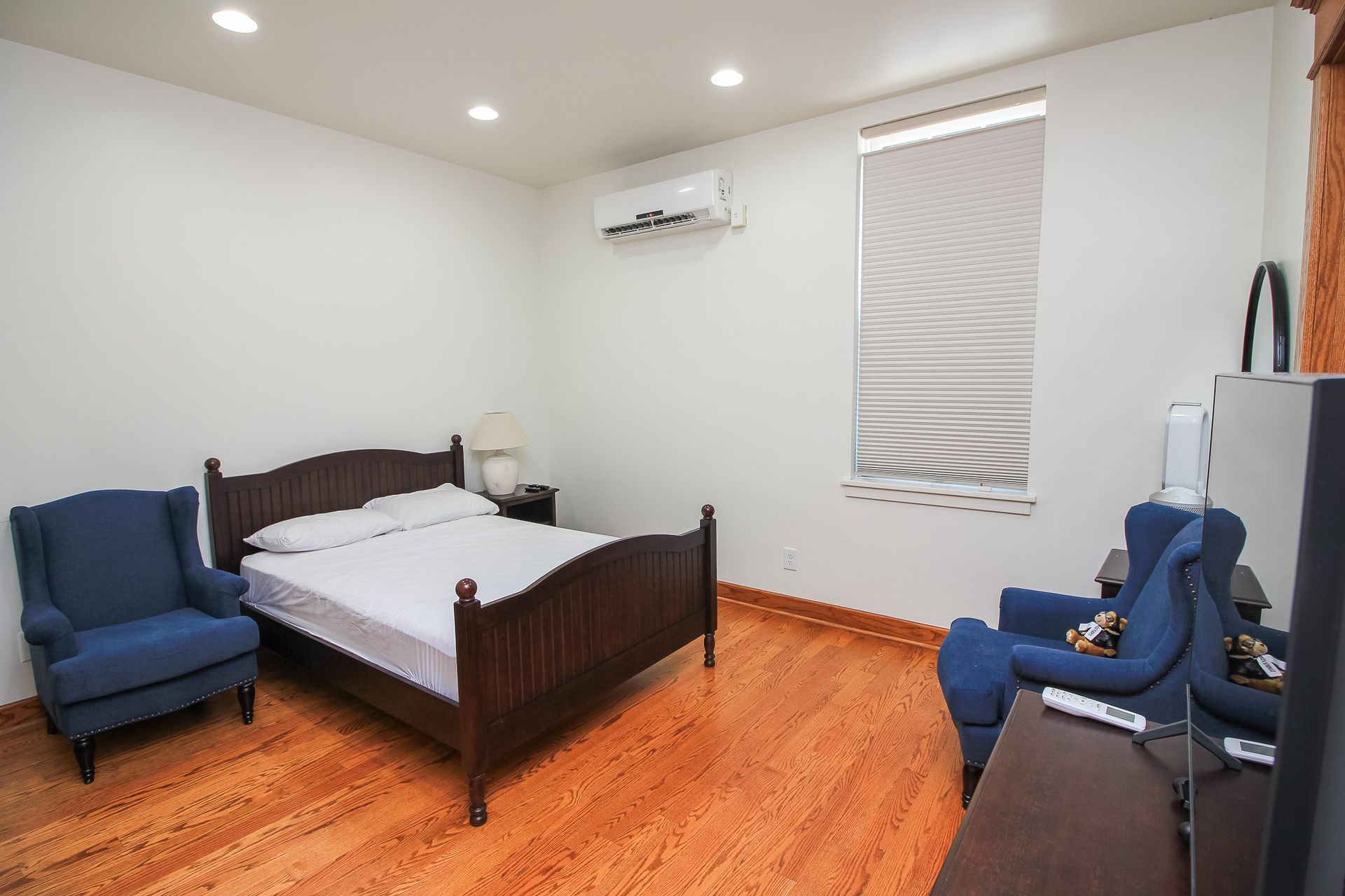 Bedroom with dark wood bed, blue chairs, hardwood floor, white walls, and window blinds