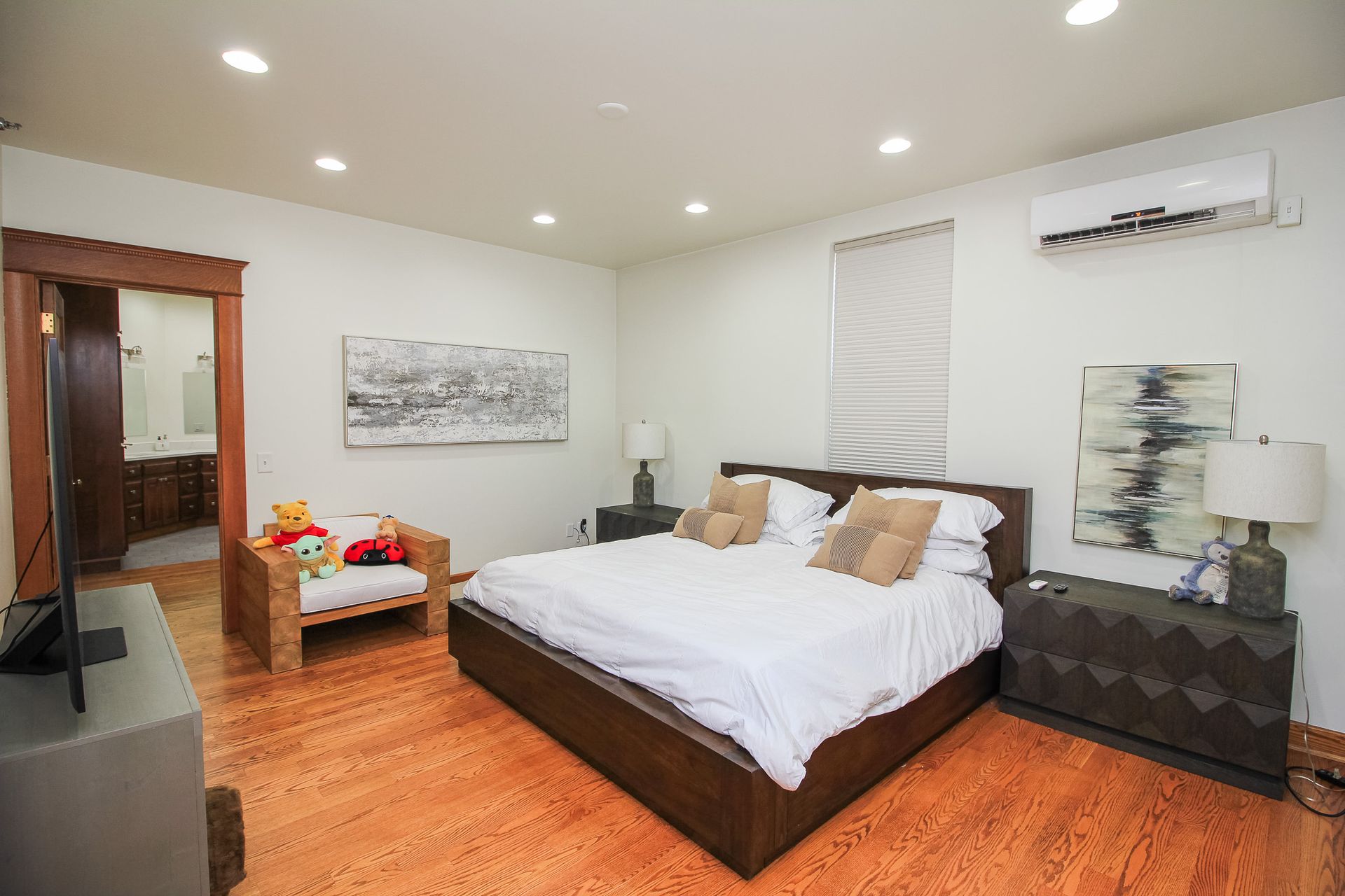 Spacious bedroom with a king bed, orange wood floor, sofa, wall art, and window air conditioner.