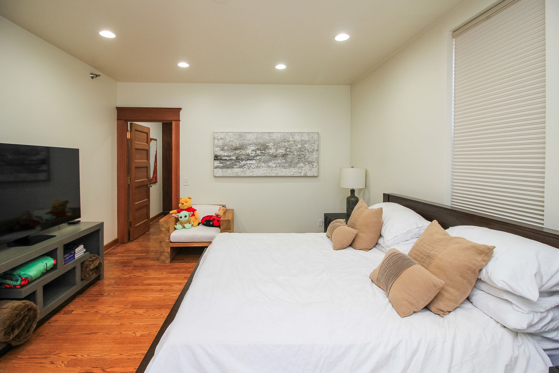 Bedroom with a large bed, TV, and warm wood floors, lit by recessed ceiling lights.