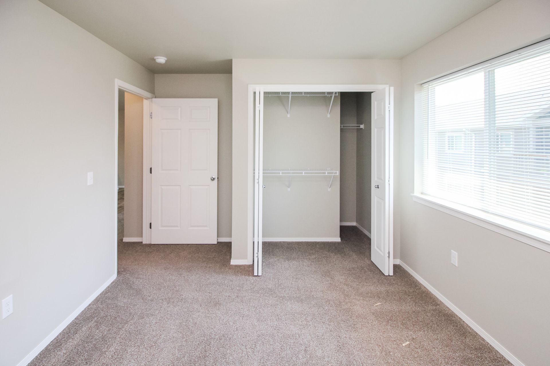 Empty beige bedroom with carpet, closet, and a window letting in daylight