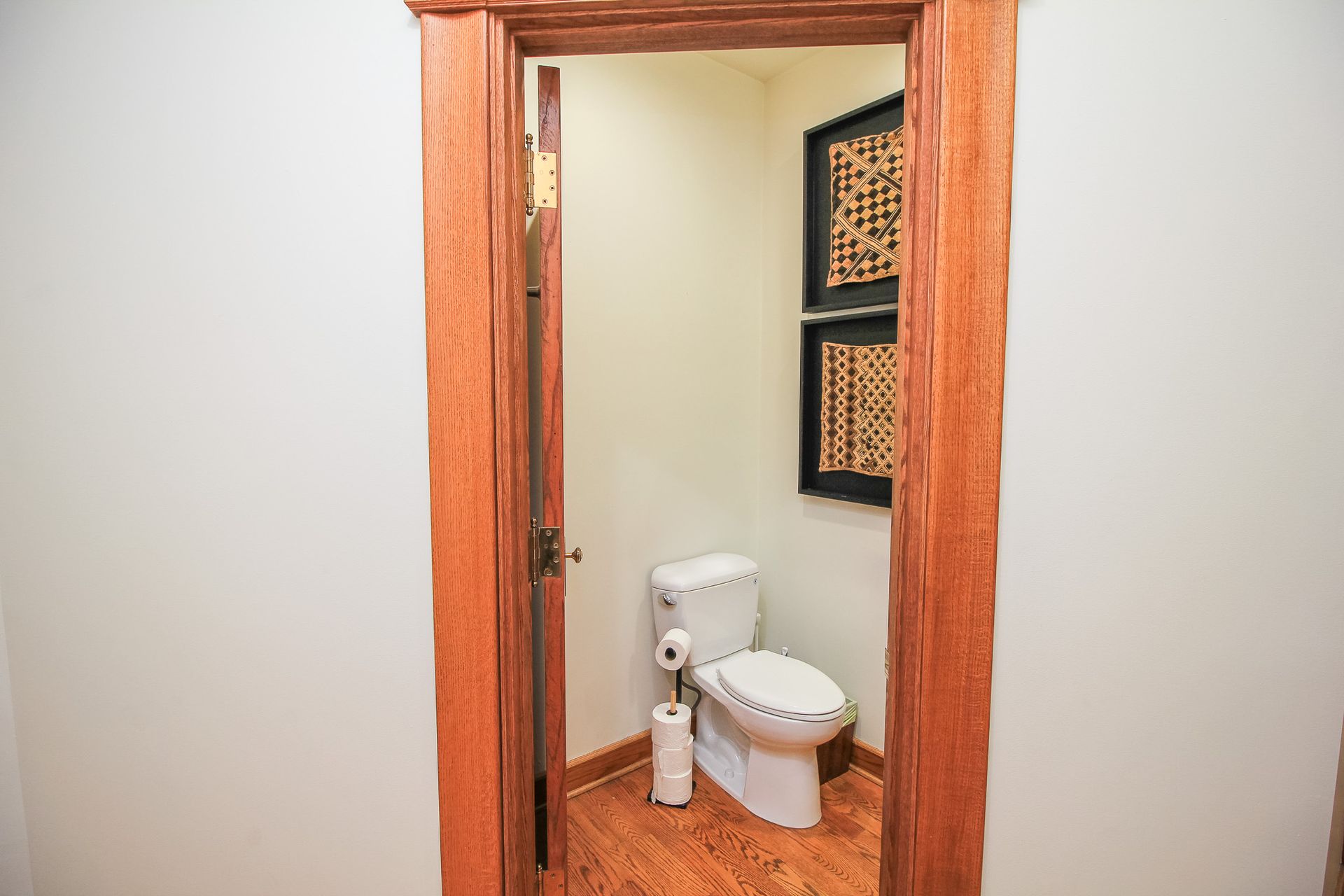 Small bathroom with a white toilet, wood trim, and framed wall art.
