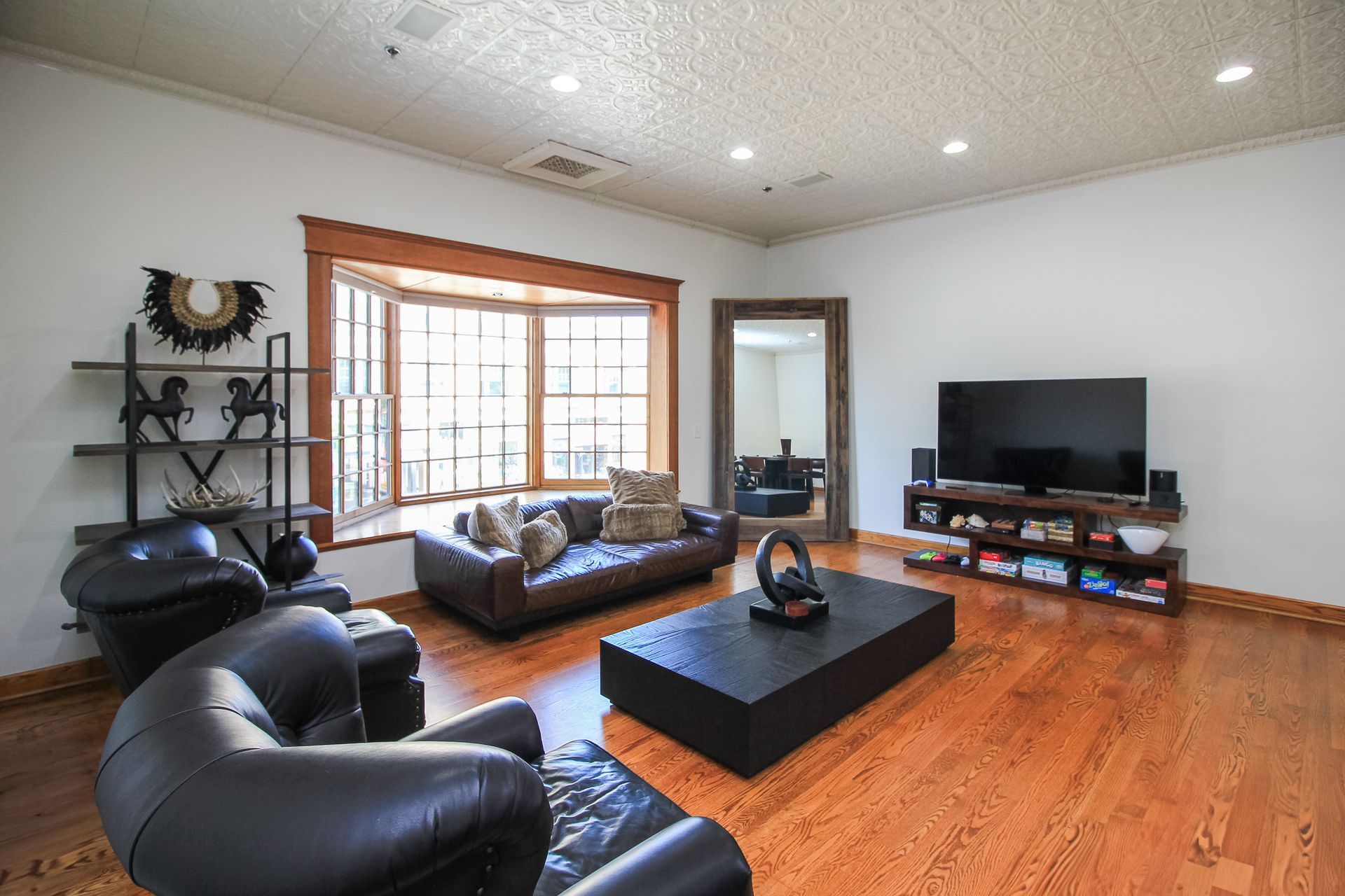 Spacious living room with leather chairs, sofa, coffee table, TV, and large window with hardwood floors