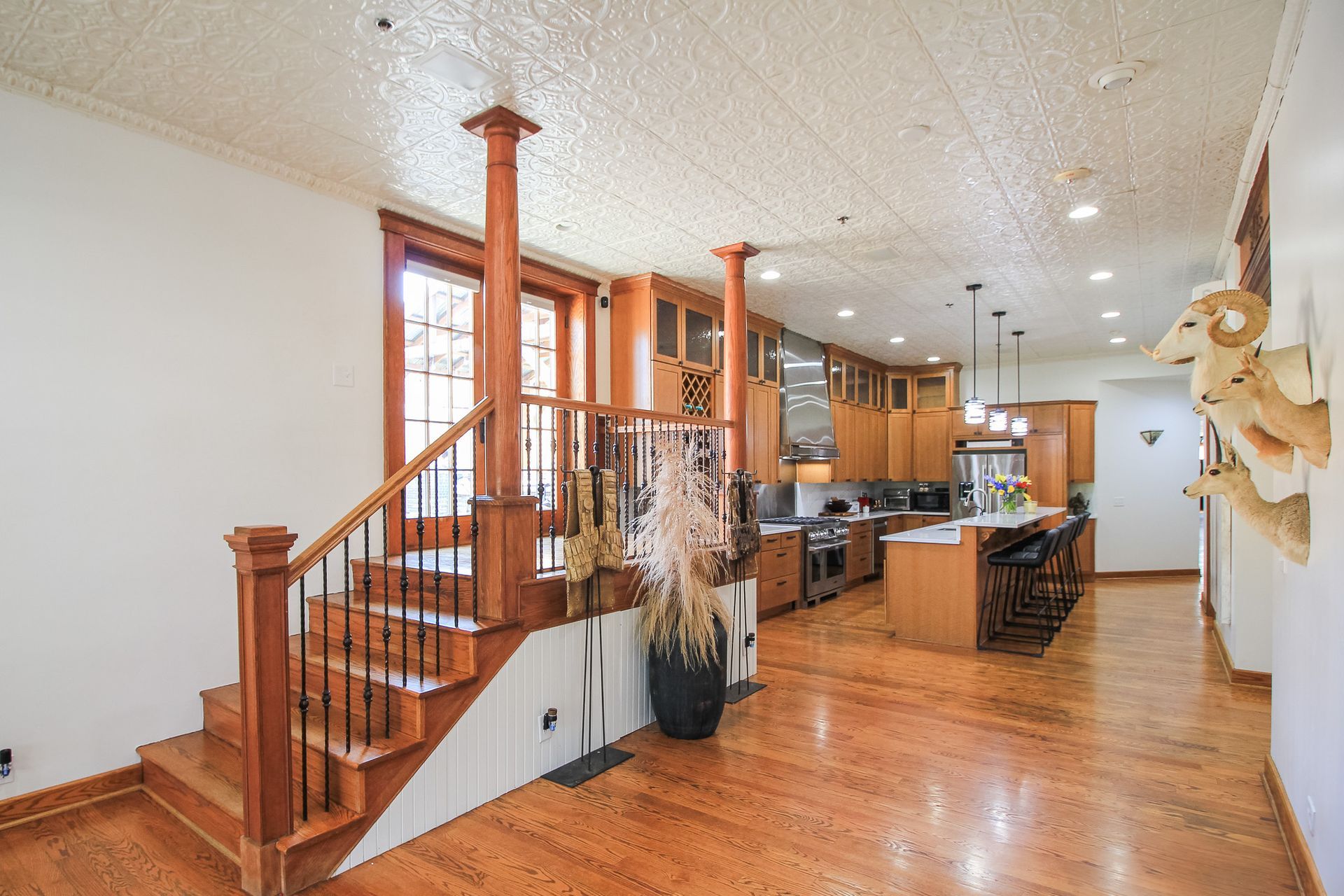 Open-concept kitchen and staircase with warm wood floors, white walls, and large windows