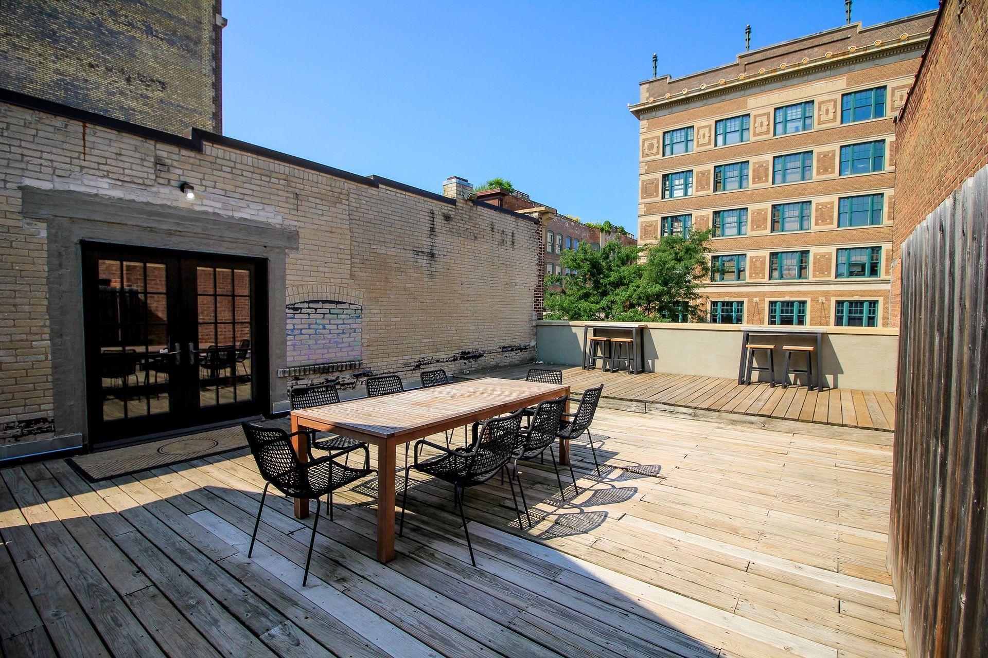 Rooftop patio with wooden table and chairs, brick walls, and a city building in the background