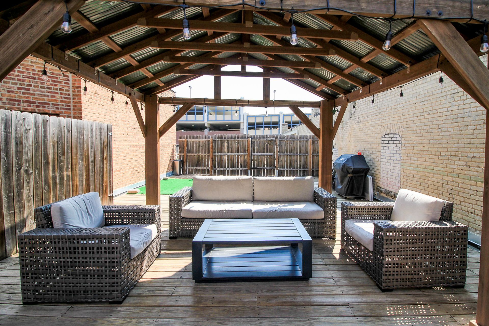 Covered backyard patio with wicker seating, coffee table, and wooden deck under a pitched roof
