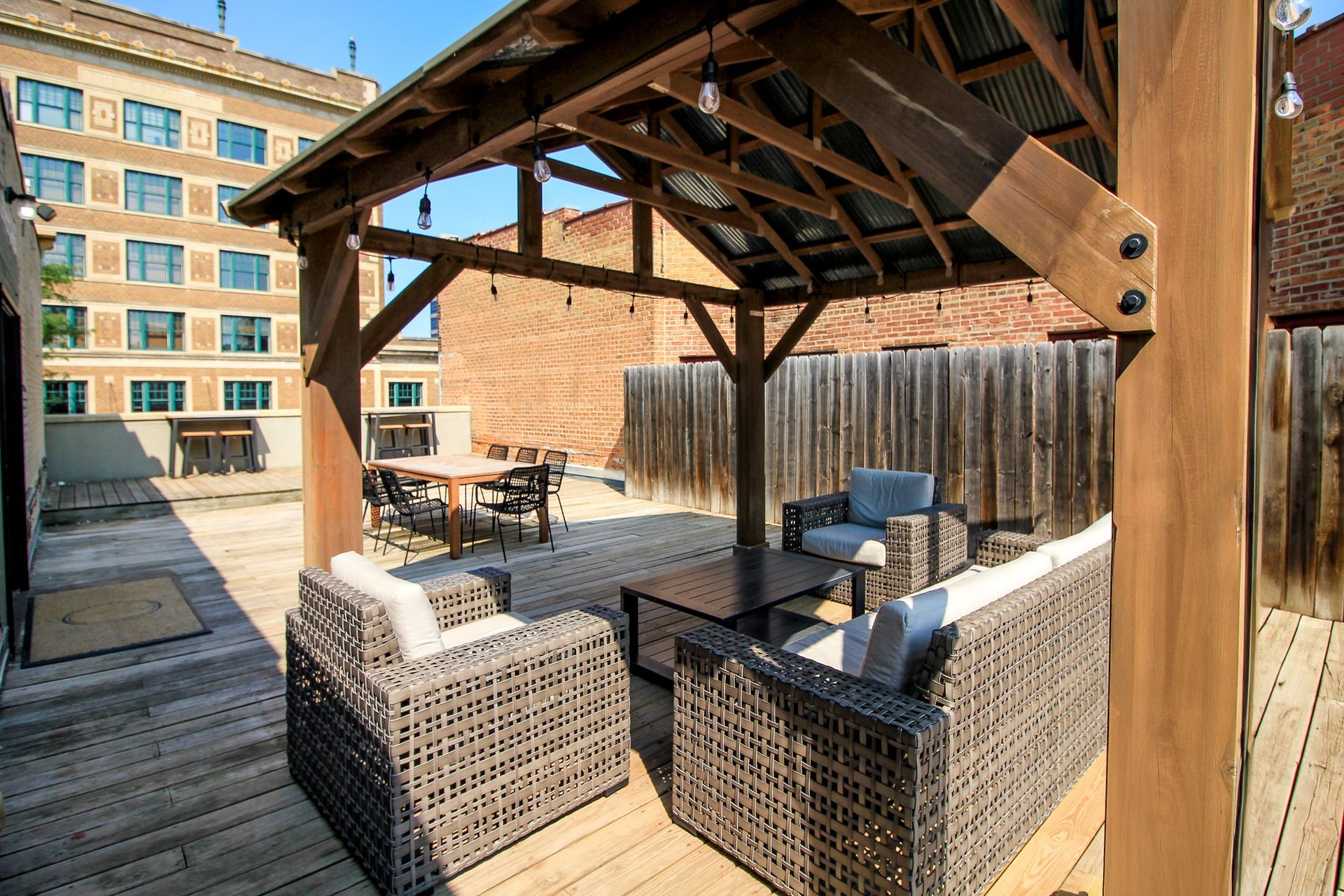 Rooftop patio with wicker seating under a wooden pergola, city buildings in the background