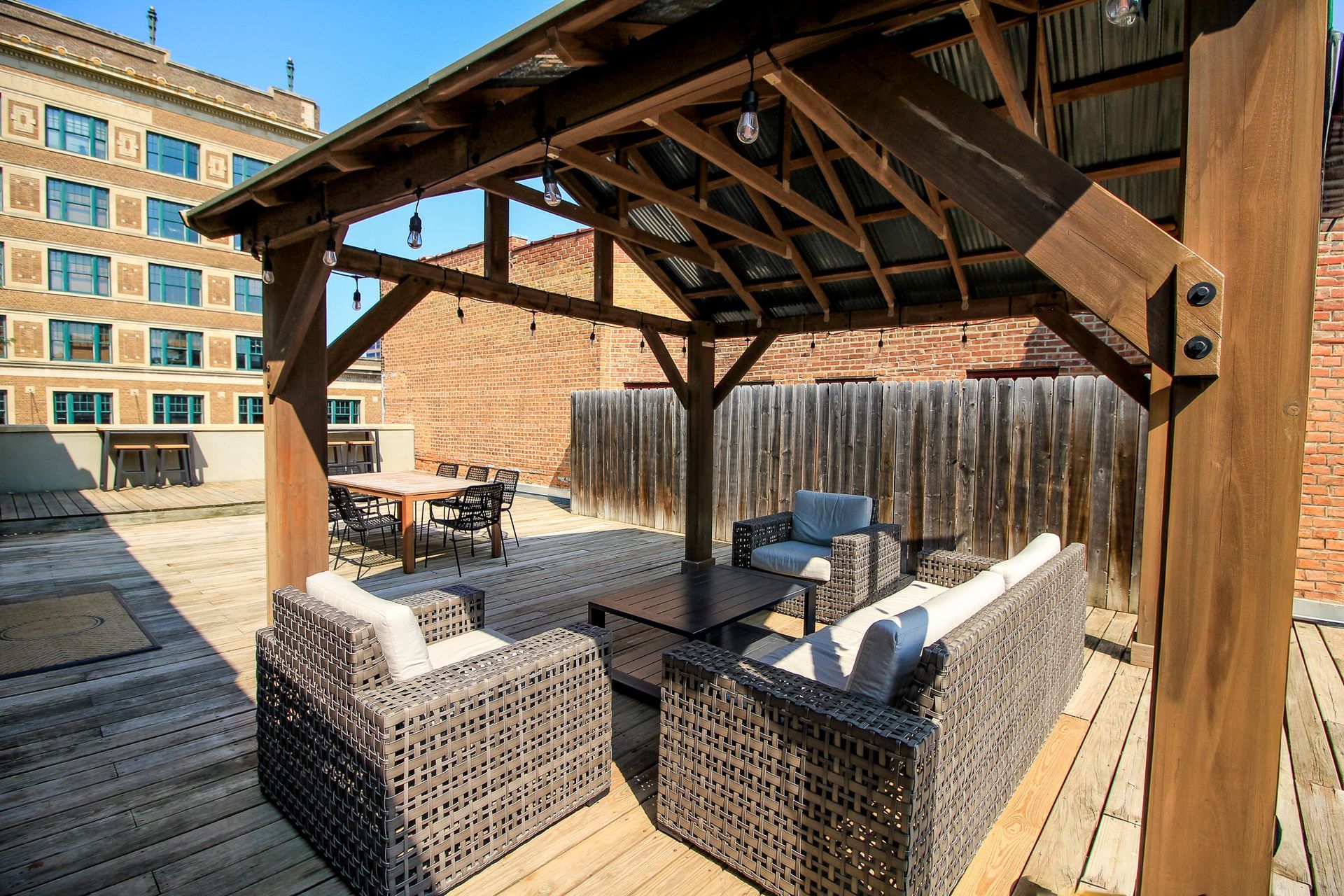 Covered rooftop patio with wicker sofas and cushioned seating on a wooden deck
