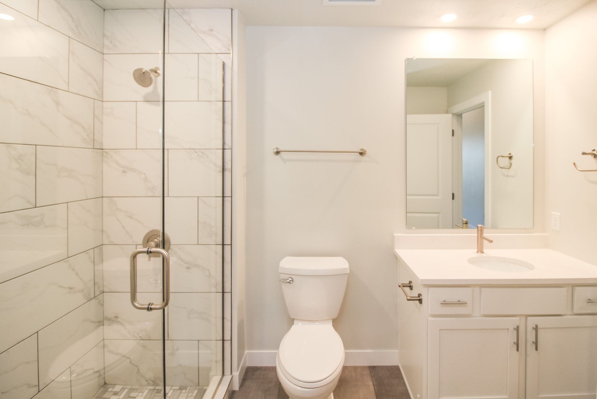 Bright white bathroom with glass shower, toilet, and vanity sink with mirror