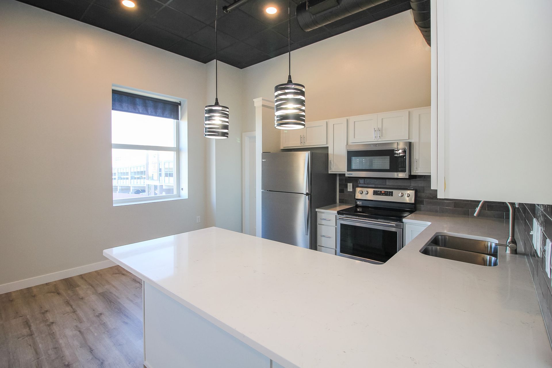 Modern kitchen with white island, stainless steel appliances, black ceiling, and pendant lights.