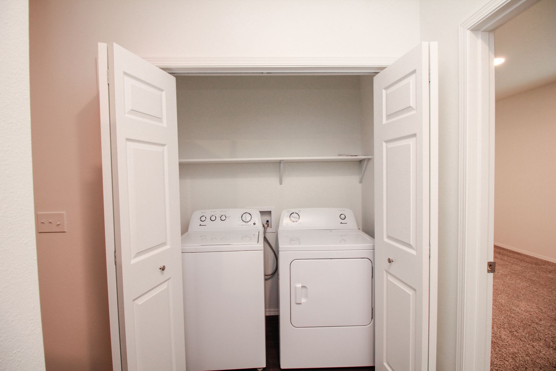 Laundry closet with stacked washer and dryer beside a wall-mounted electrical panel and open bi-fold doors