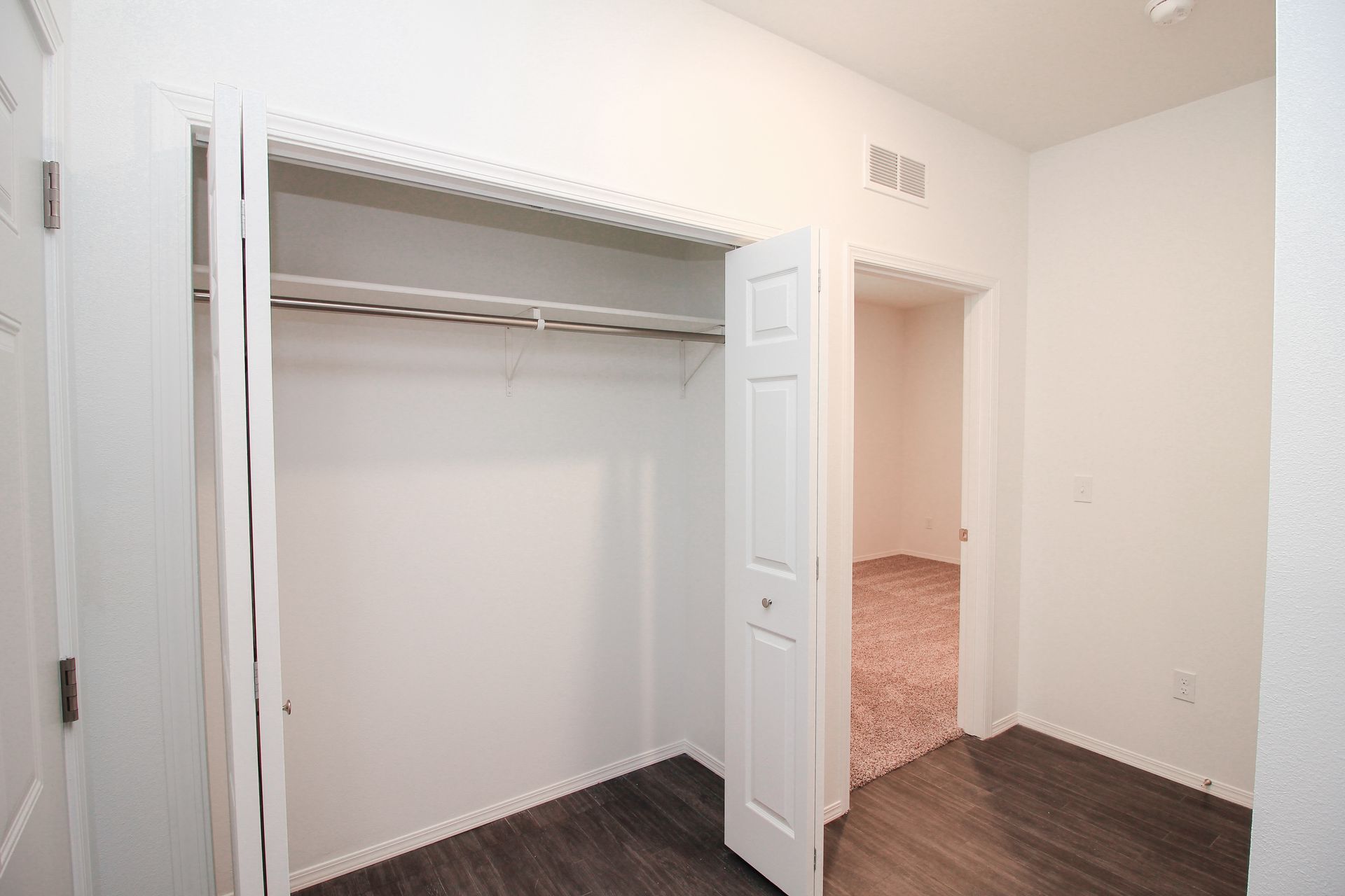 Empty closet with white walls, wire shelf, open louvered doors, and dark wood flooring.