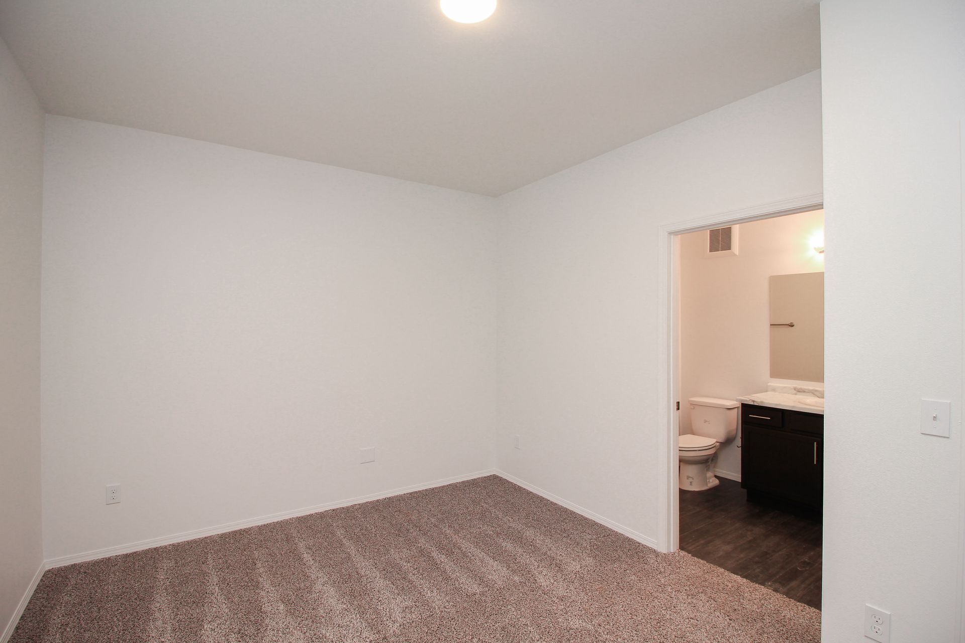 Empty beige bedroom with carpet and an open doorway to a bathroom at right