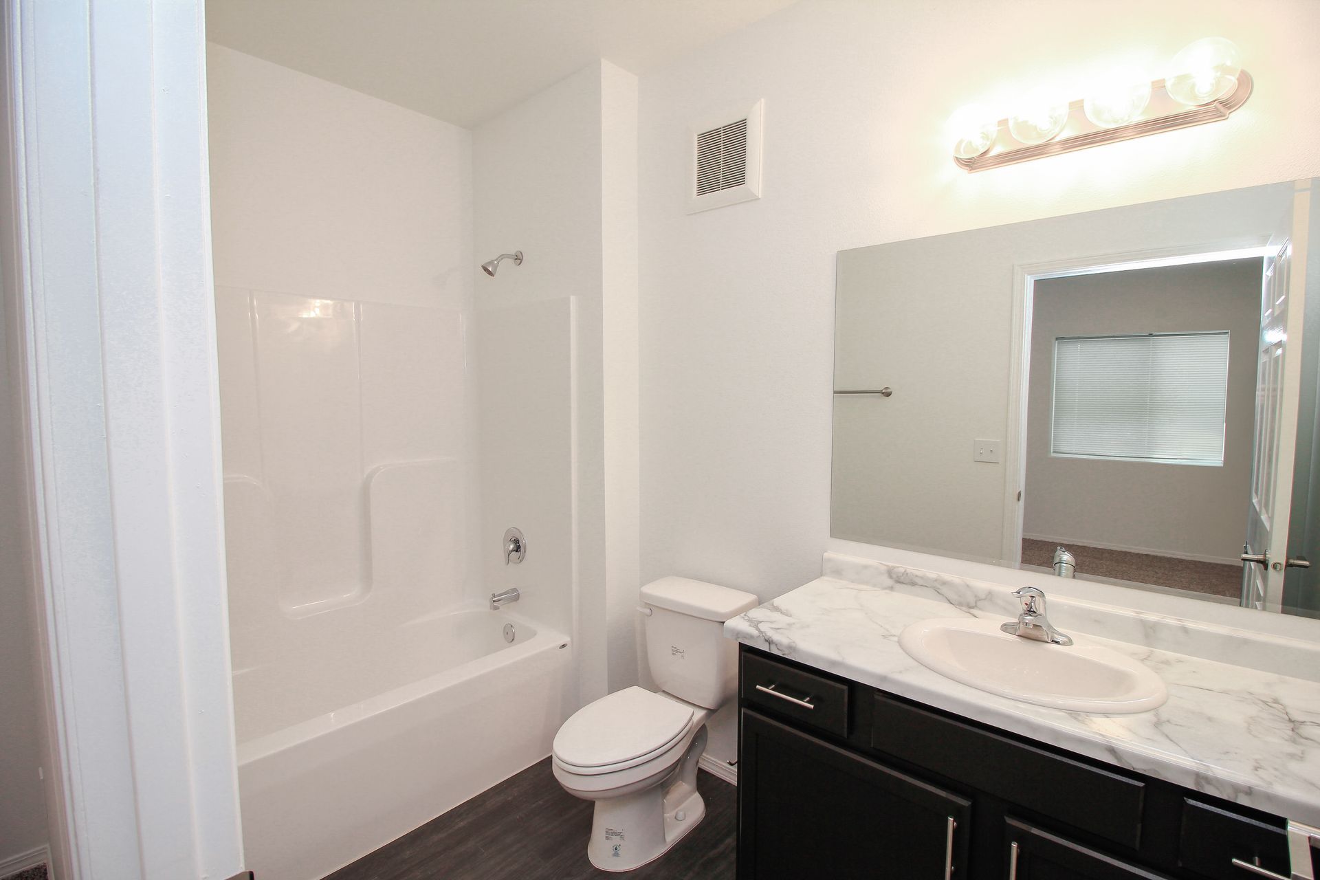 Bright white bathroom with tub, toilet, and dark vanity under a large mirror.