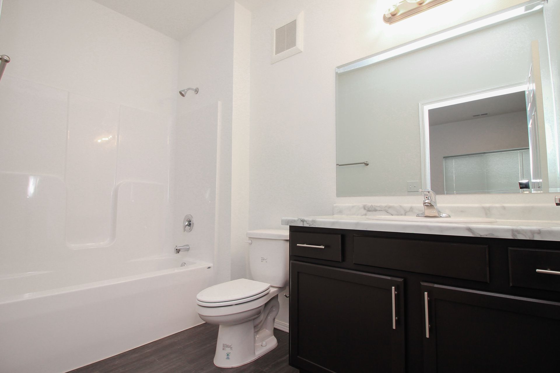 Modern bathroom with white tub, toilet, and dark vanity with large mirror