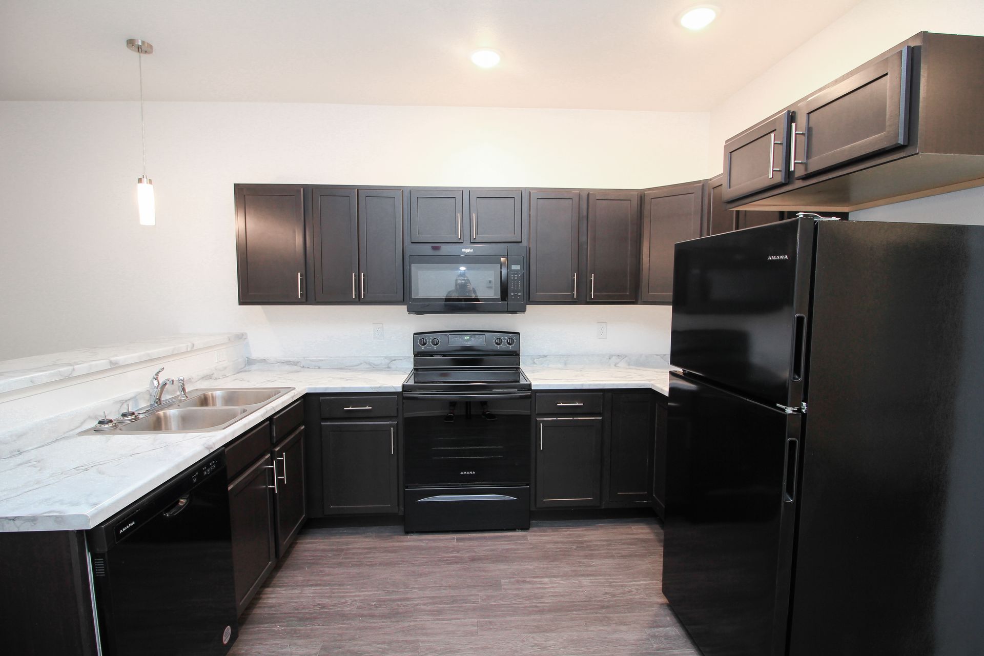 Modern kitchen with dark cabinets, black appliances, and white countertops.