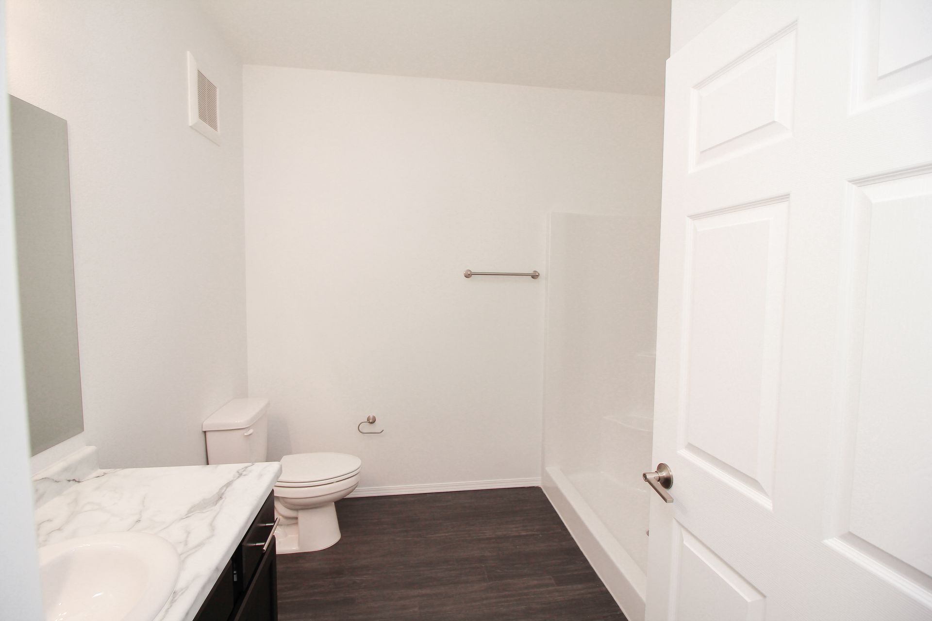 Modern white bathroom with toilet, vanity sink, towel bar, and dark wood floor