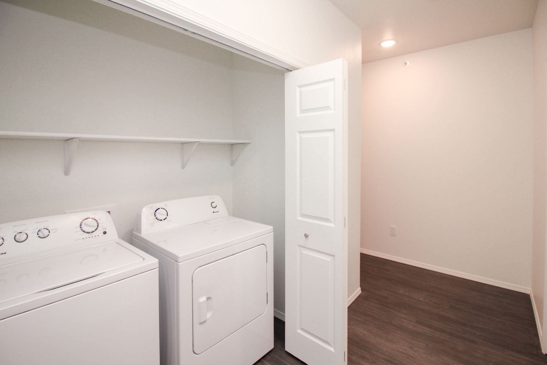 Laundry room with washer and dryer, white shelves, and an open door to a hallway.