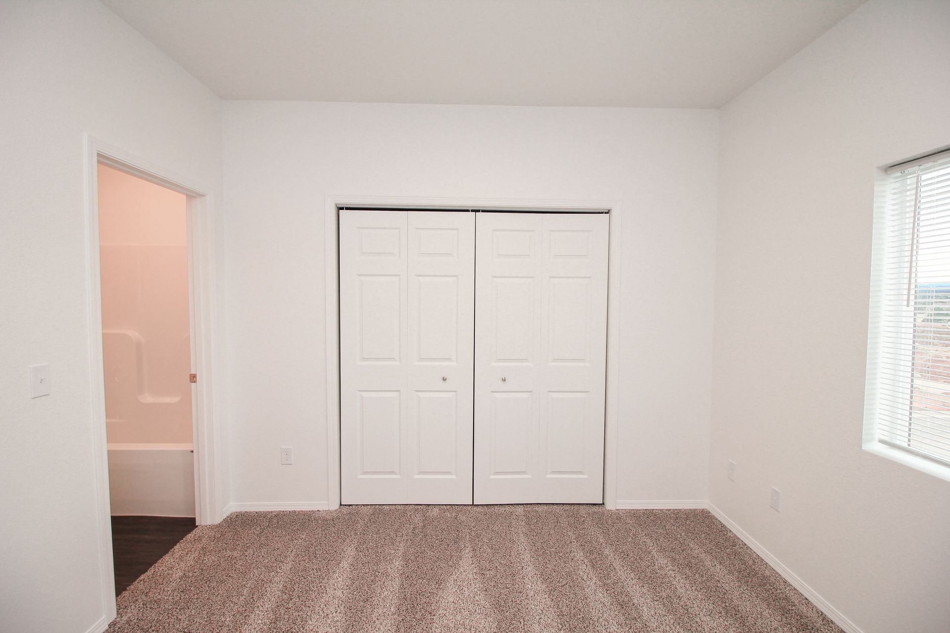 Empty white room with dark wood floors, ceiling fan, and sliding glass doors with vertical blinds