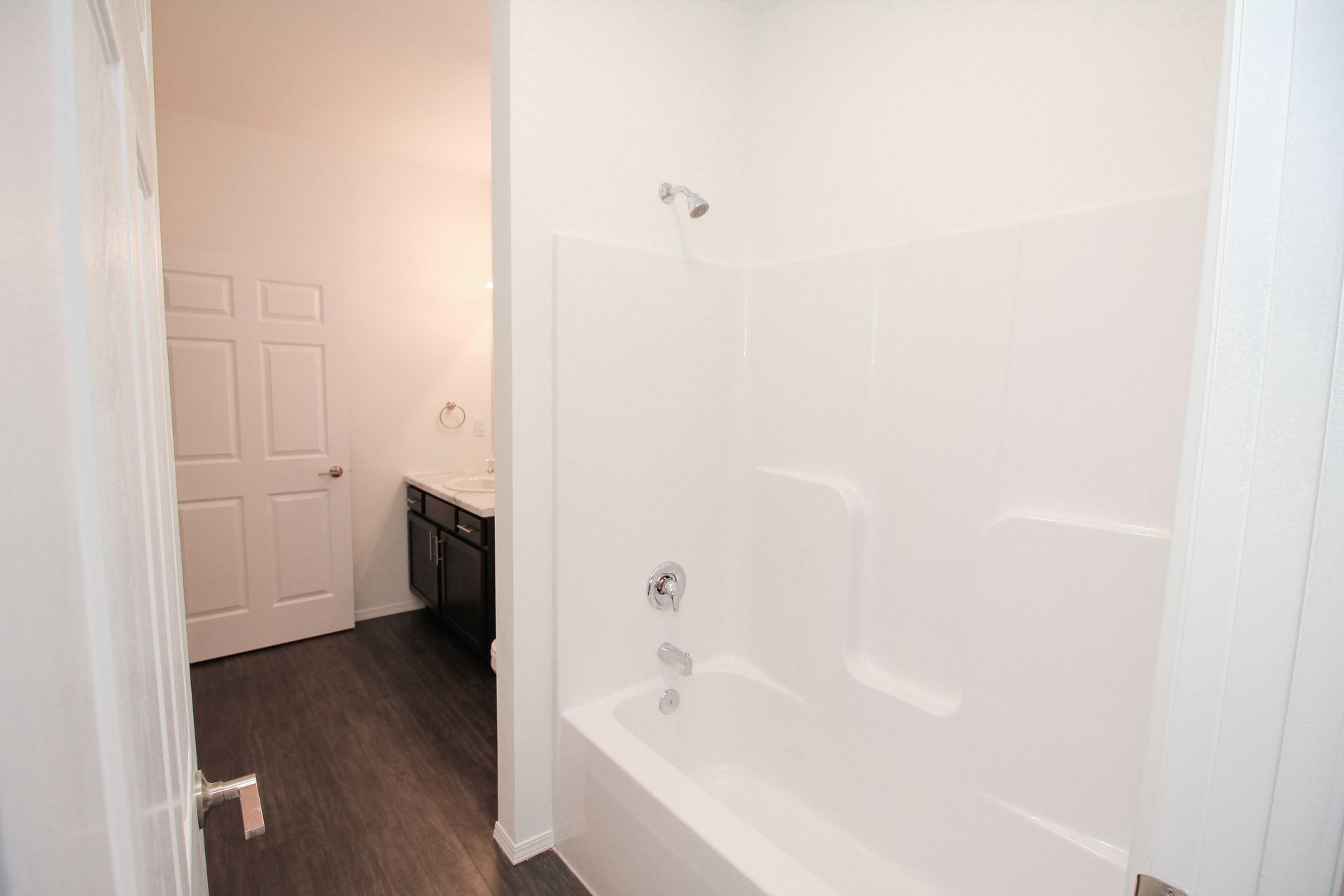 Modern bathroom with black vanity, white countertop, mirror, toilet, and hallway entry to a carpeted room