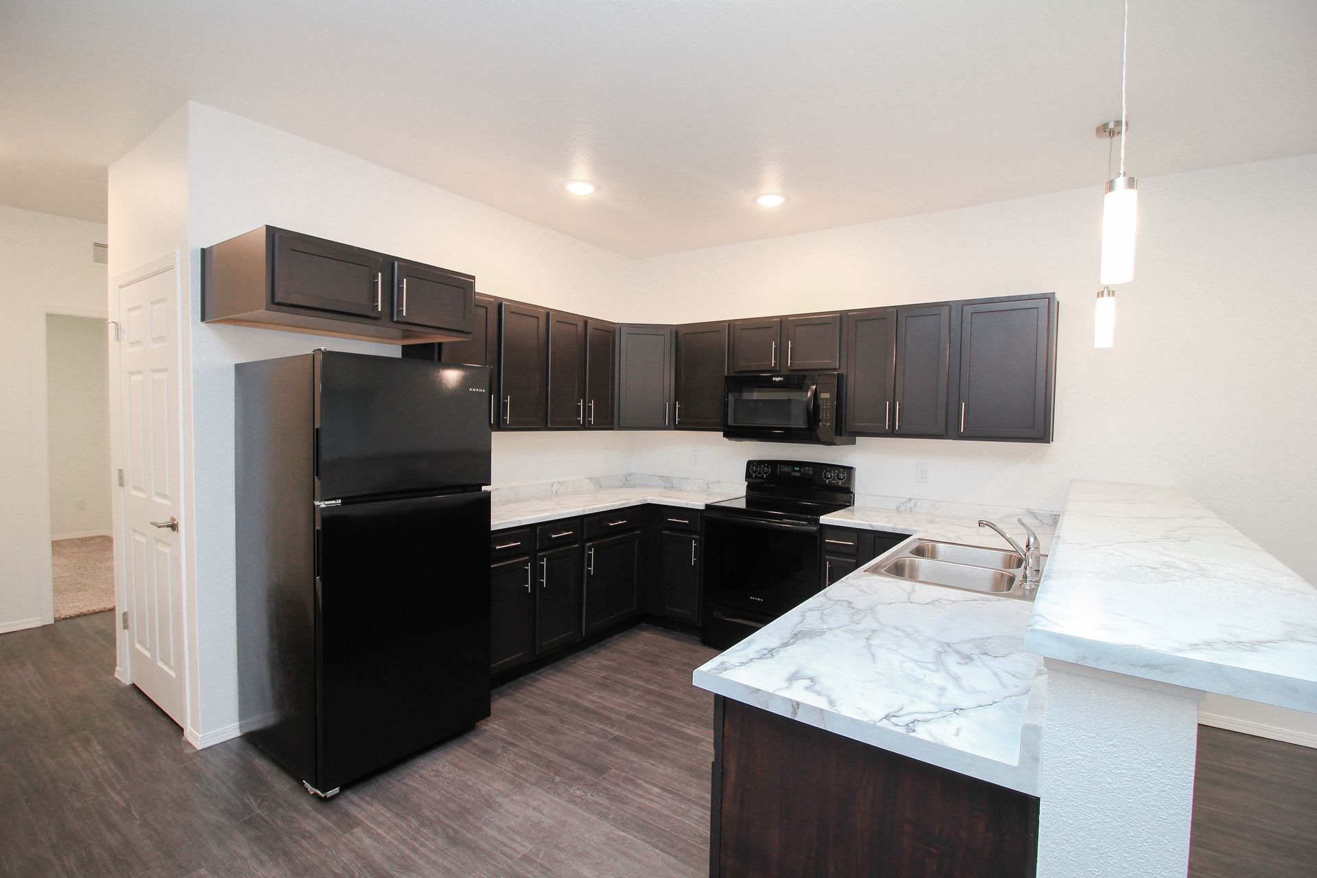 Modern kitchen with black cabinets, dark appliances, marble island, and wood-look flooring