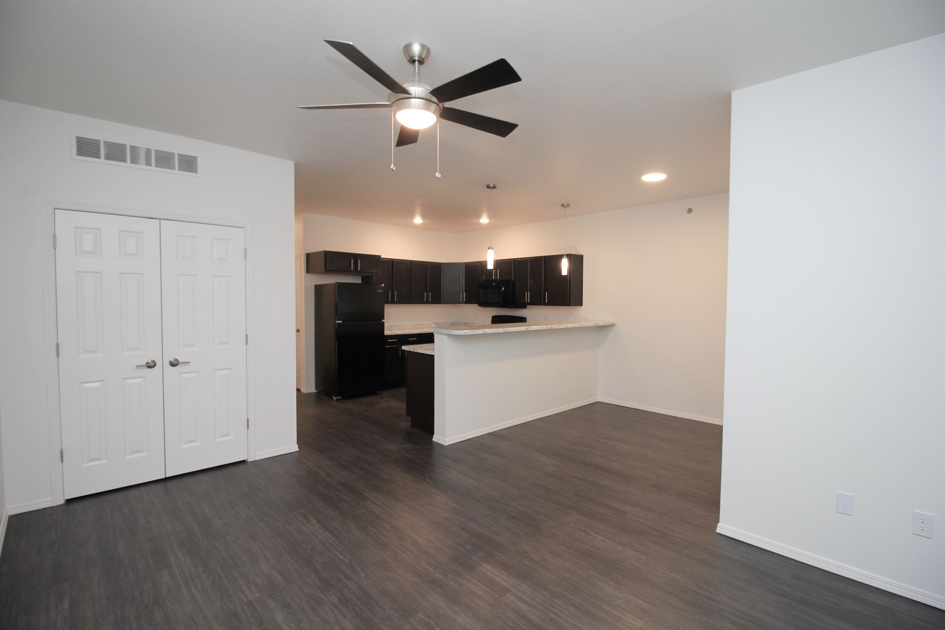 Empty apartment living area with dark cabinets, white counters, and sliding glass doors