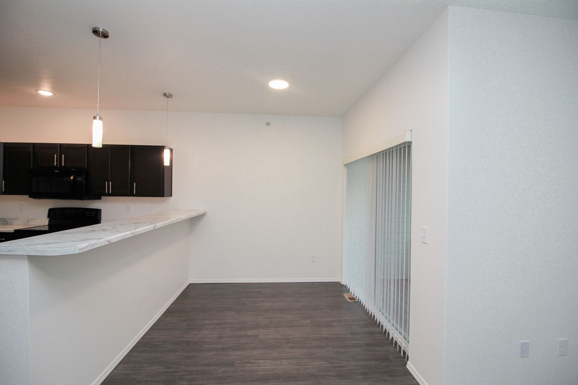 Empty modern kitchen with dark cabinets, black appliances, white marble-style counters, and a peninsula island.