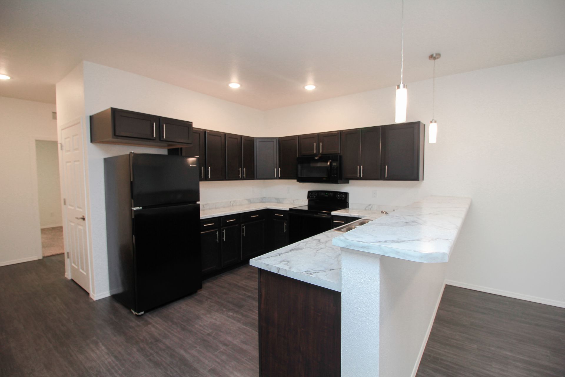 Modern kitchen with black appliances, dark cabinets, and a white marble breakfast bar.