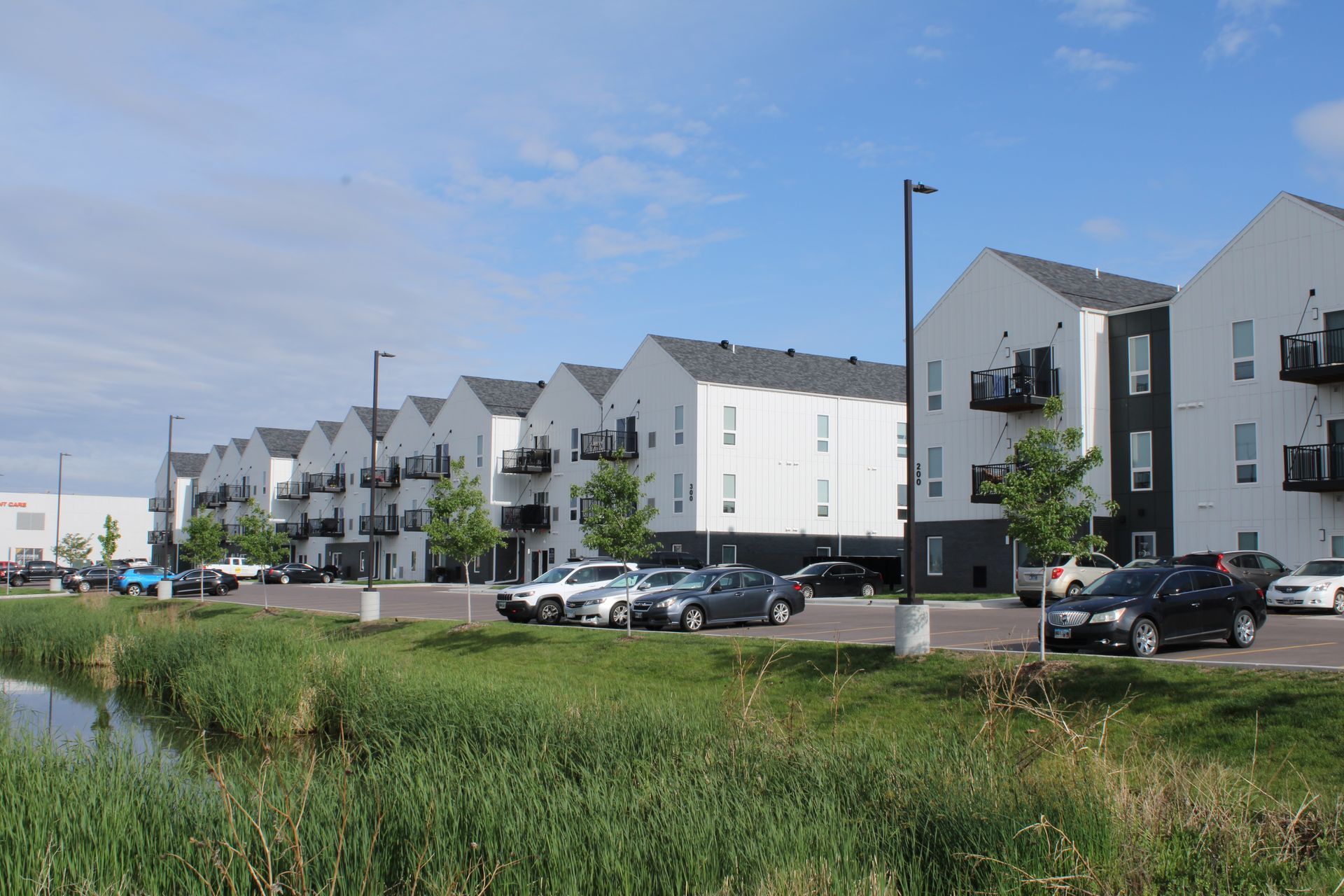 Modern apartment buildings beside a road and grassy field under a blue sky