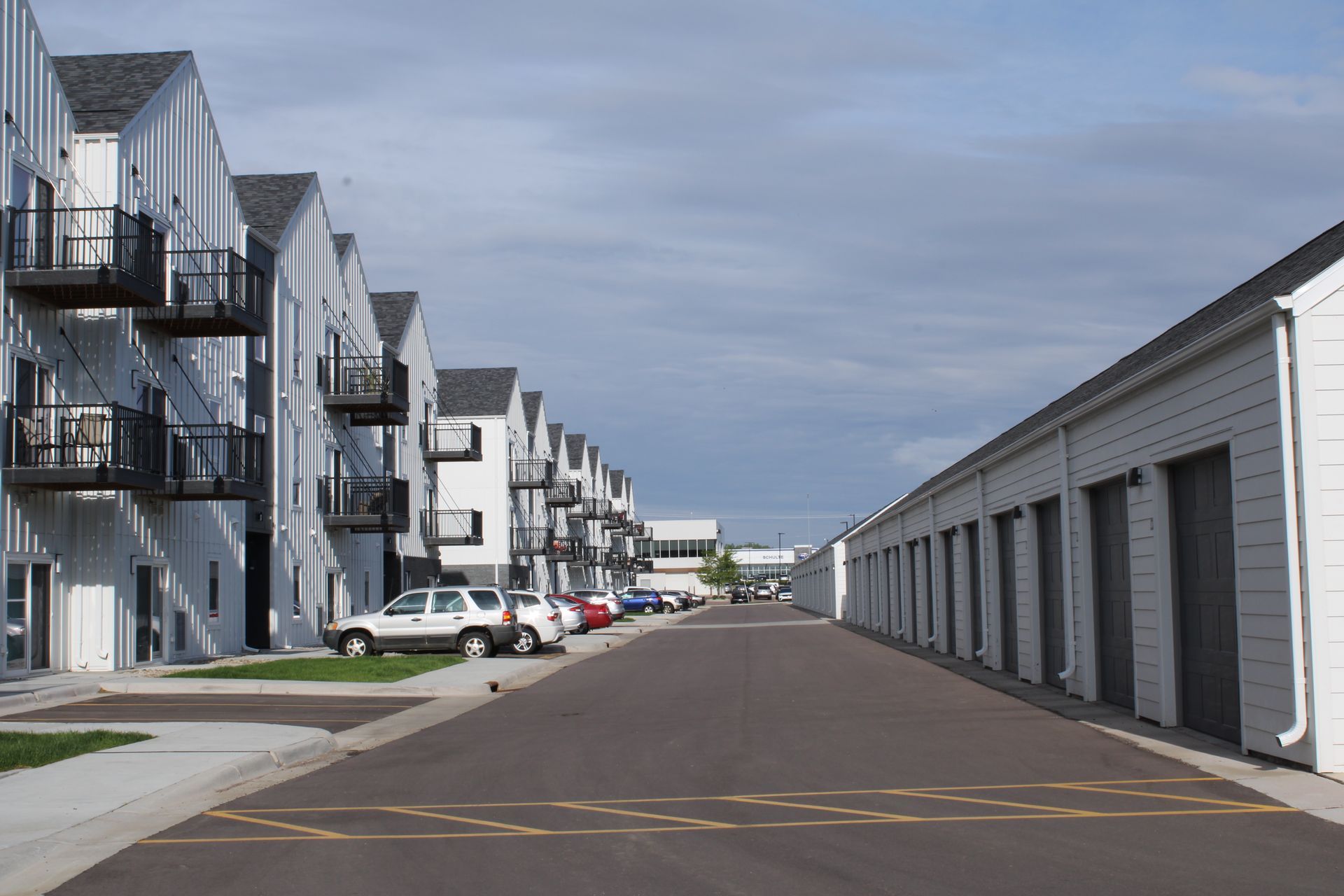 Apartment complex parking lot with white garage units and rows of balconies under a cloudy sky